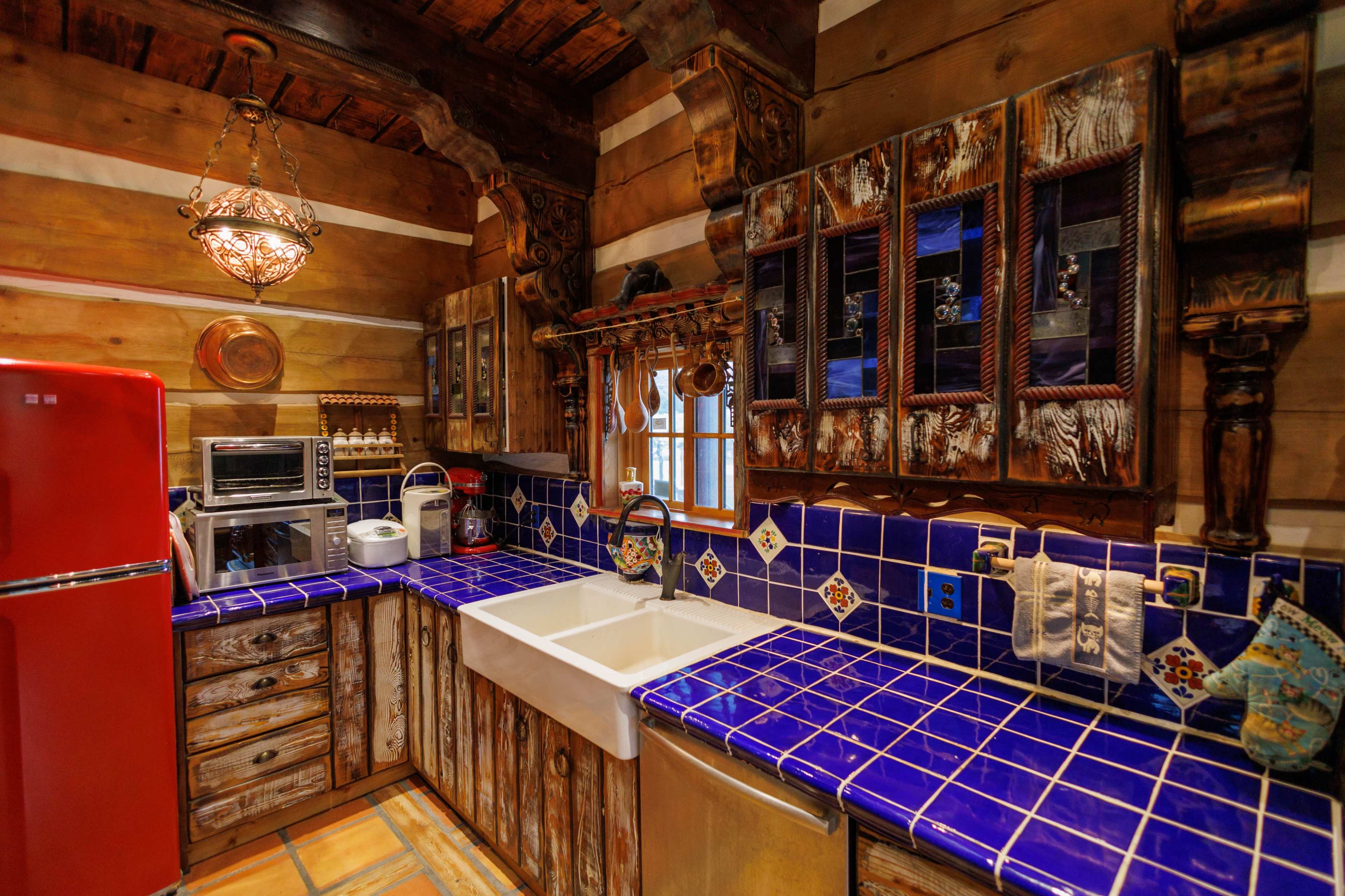The kitchen features wooden walls, a blue tiled countertop, a farmhouse sink, and a red refrigerator.