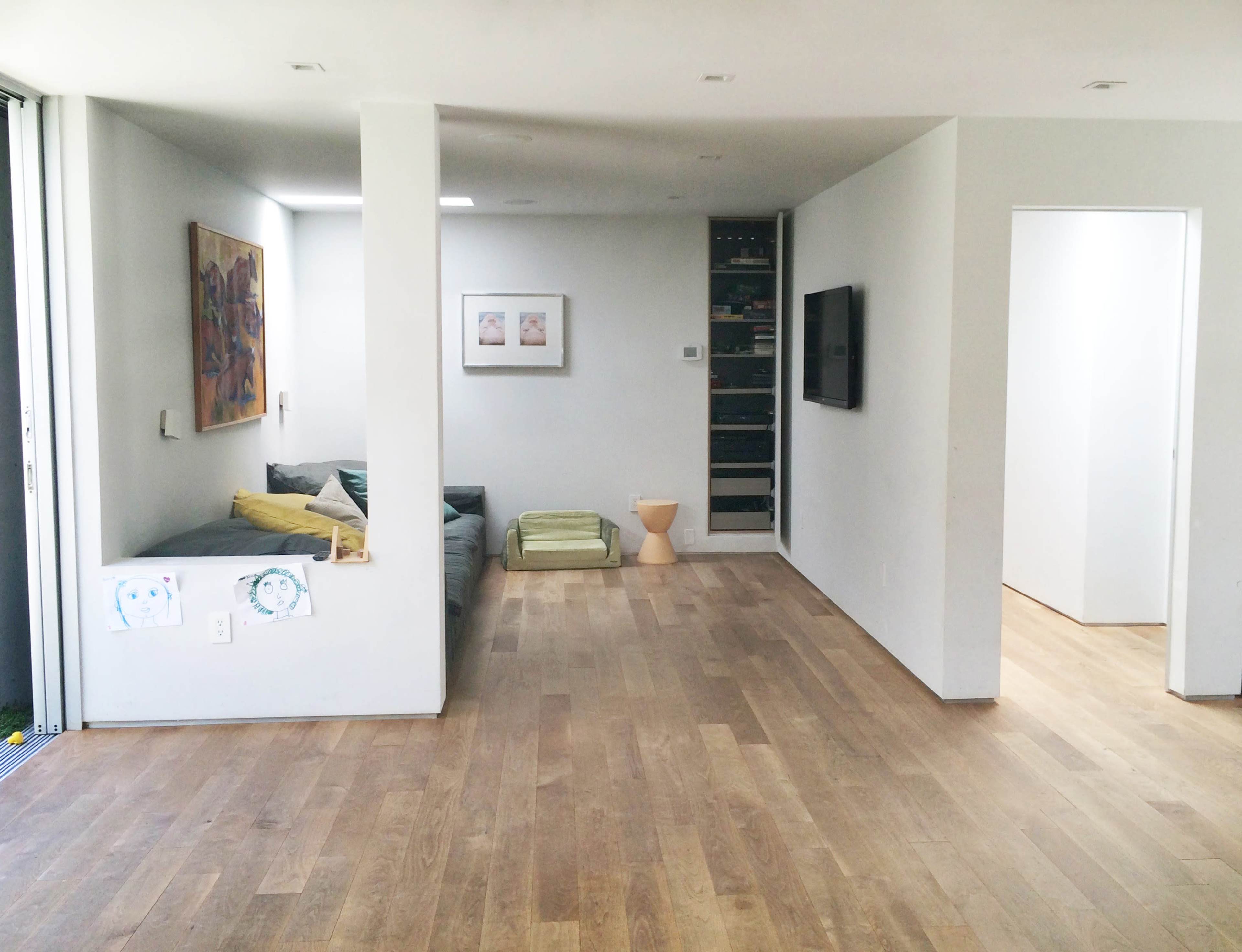 An interior space with a small seating area on the left, a wall-mounted TV, and a doorway on the right leading to another room.