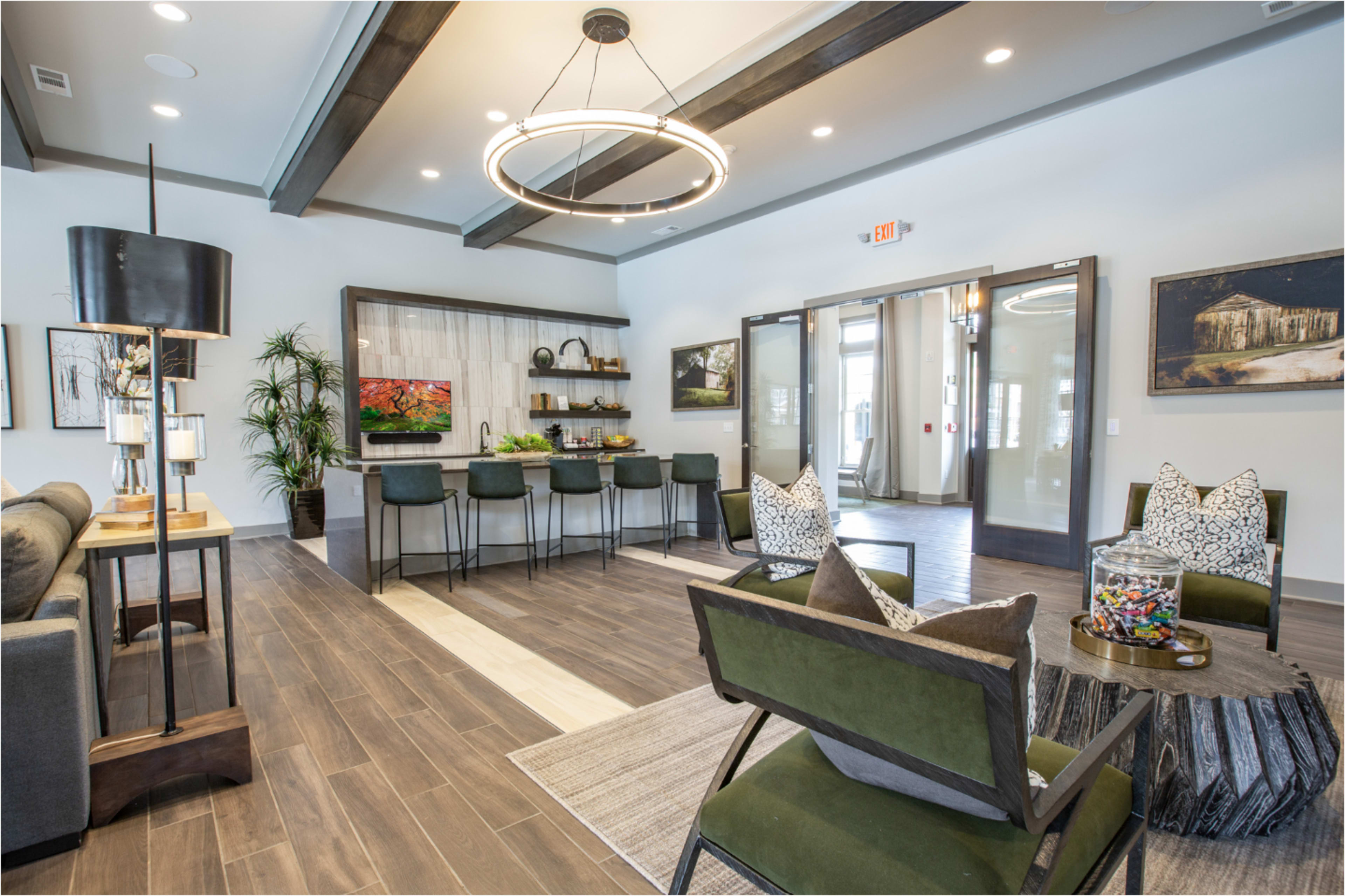 The image shows a modern communal lounge area featuring comfortable seating, a bar-style kitchen counter, and decorative artwork on the walls.