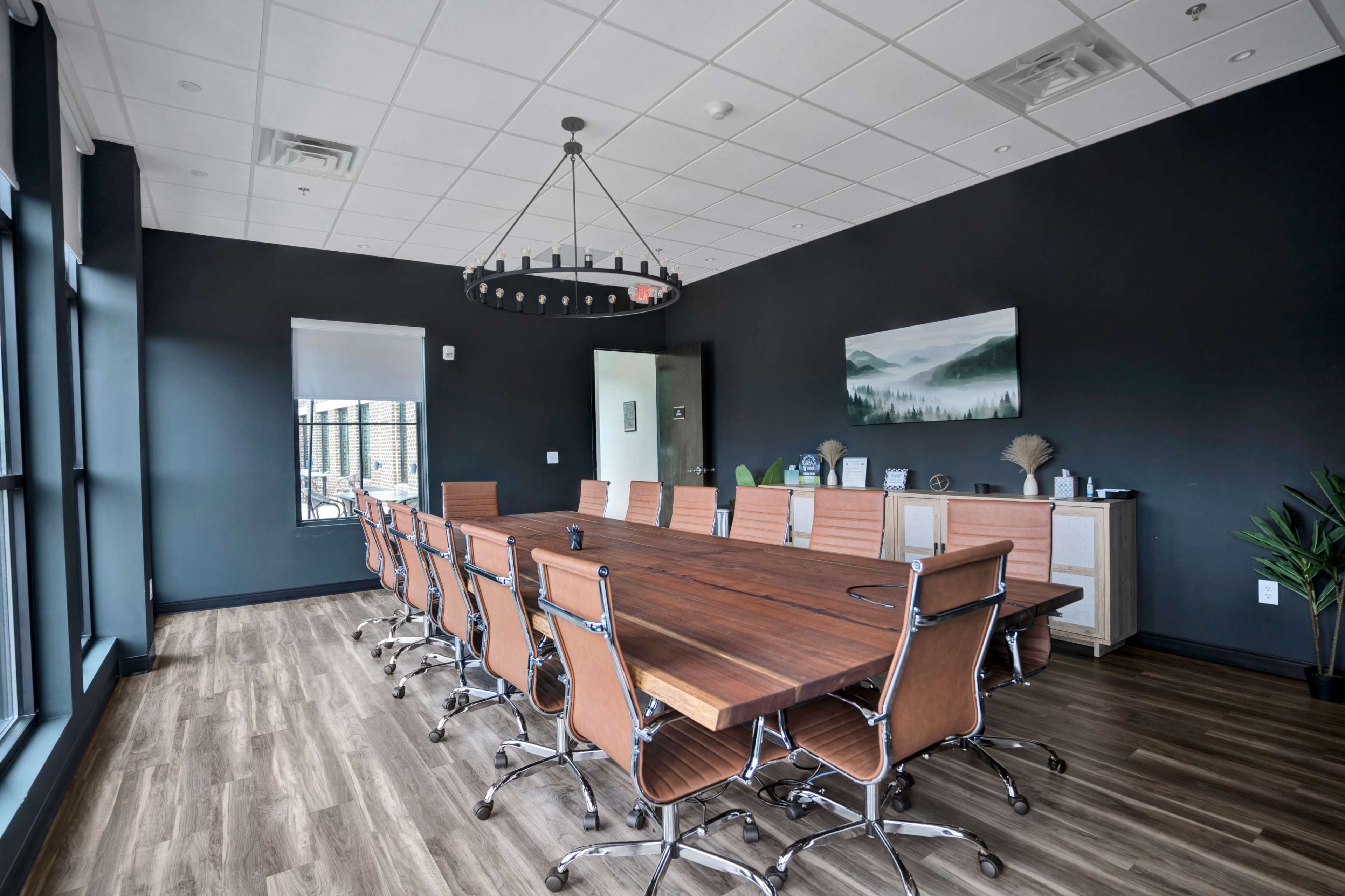 A large conference room with a wooden table surrounded by ergonomic chairs, set against a dark wall and featuring large windows.