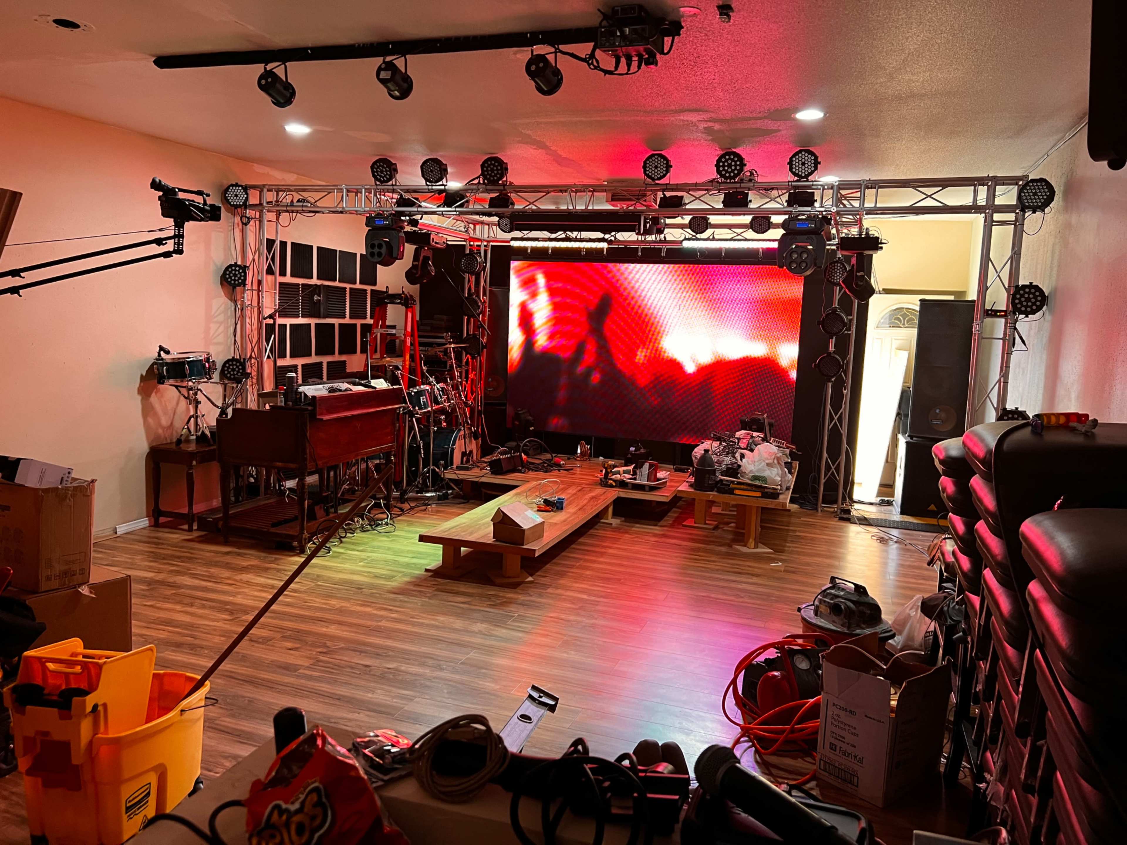 A room with a large LED screen at one end, surrounded by lighting fixtures, cables, and various equipment, with unfinished decorations and boxes scattered throughout.