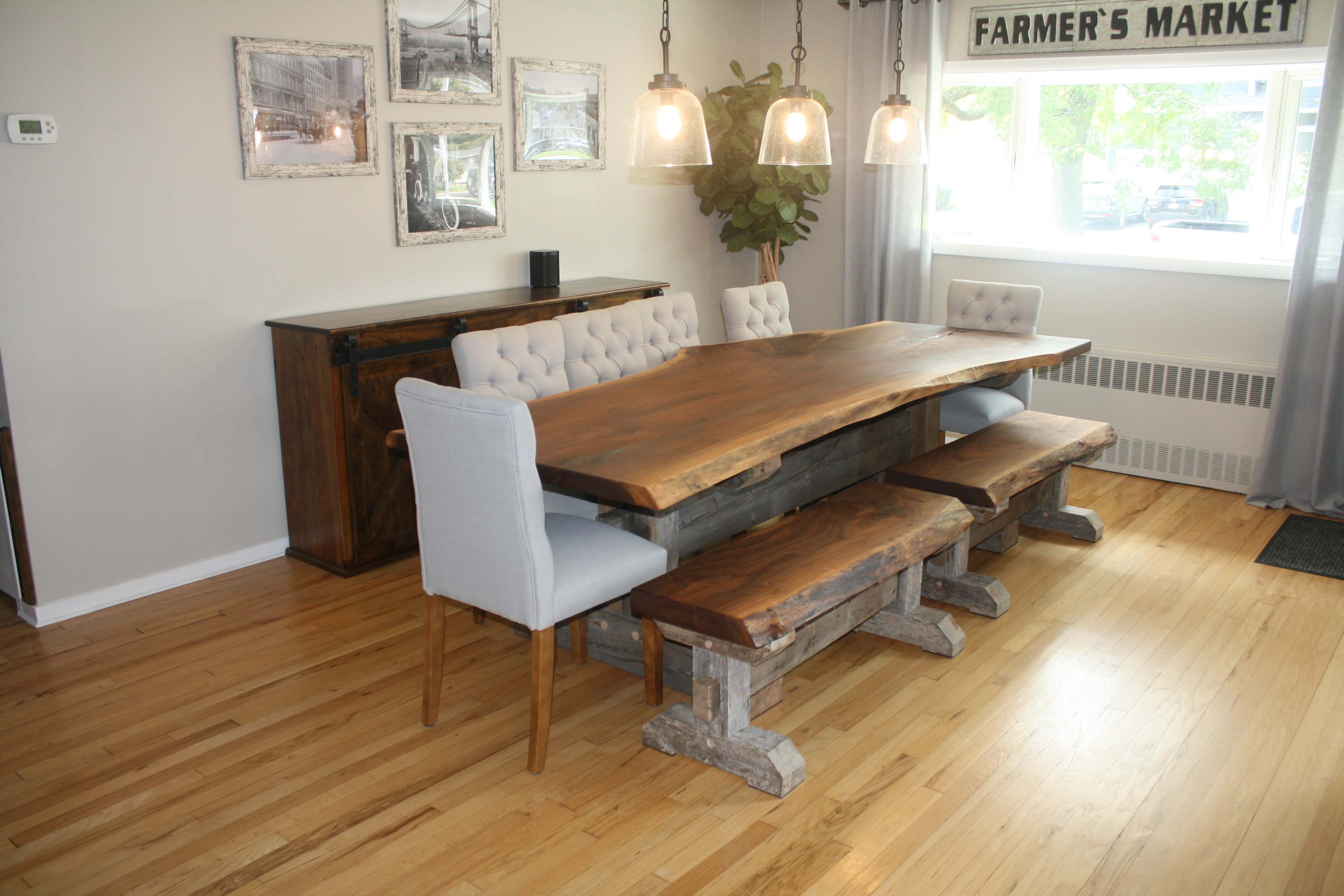 A rustic wooden dining table with benches and upholstered chairs is set in a room featuring large windows and pendant lighting.