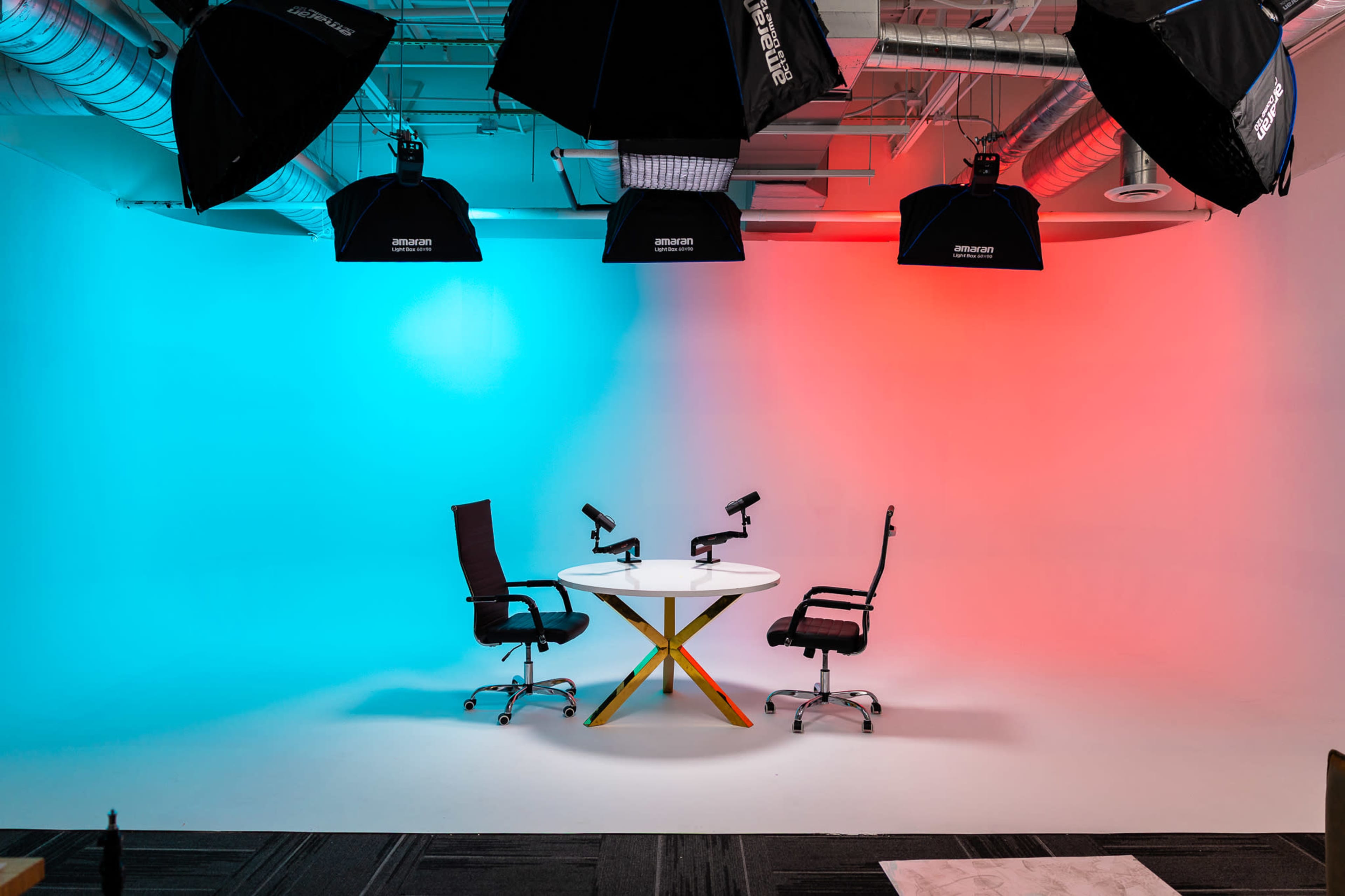 The image shows a studio setup with two chairs facing a round table, illuminated by contrasting blue and red lights in the background.