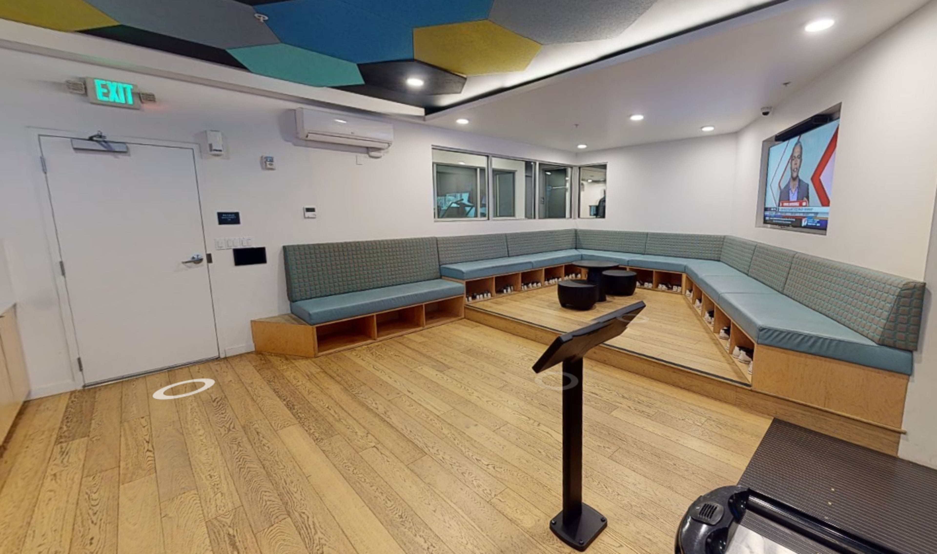 A modern lounge area with a curved seating arrangement, a flat-screen TV on the wall, and wooden flooring.