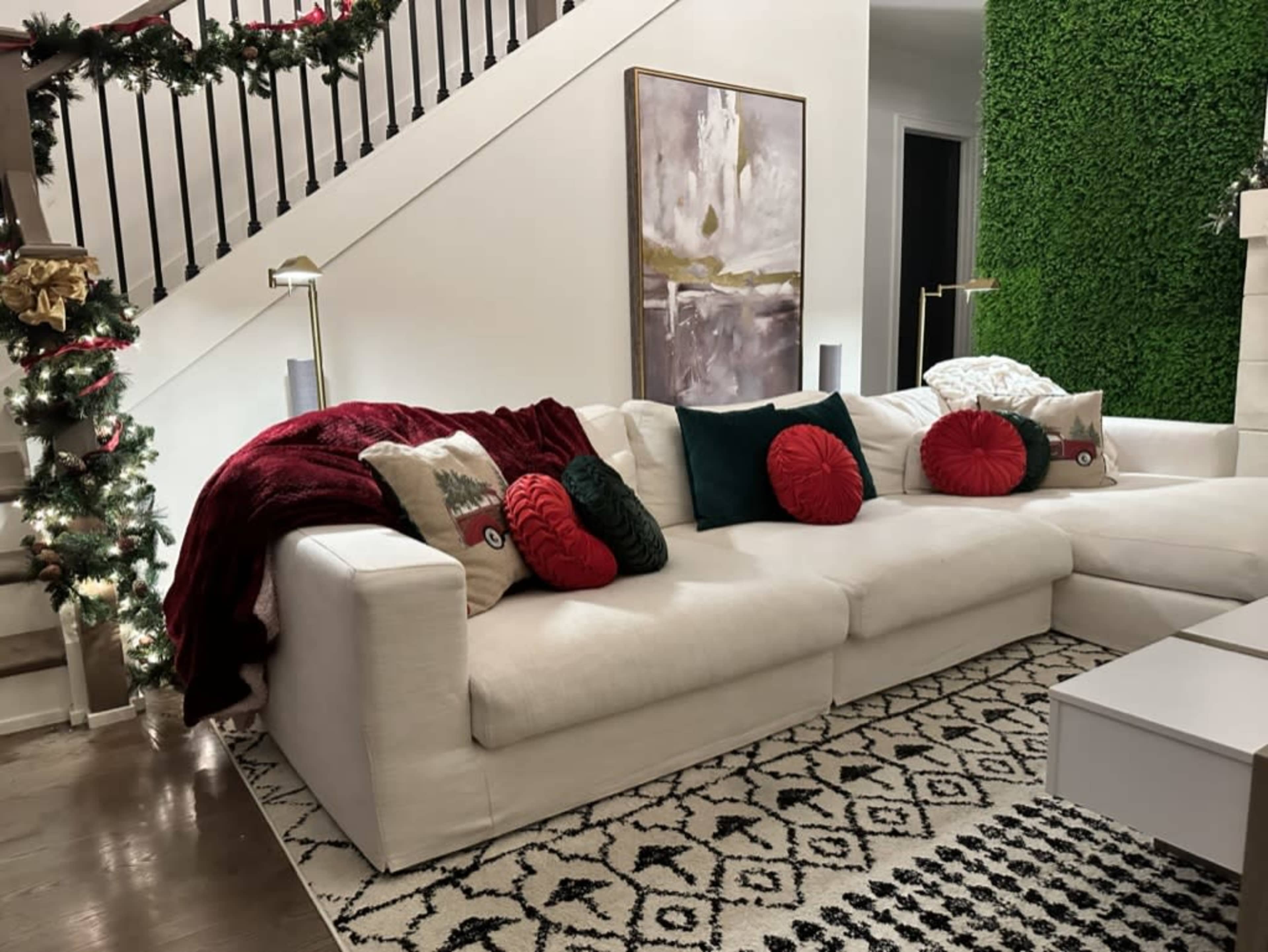 A sectional sofa adorned with red and green pillows is positioned in a spacious living area, complemented by a decorative wall and festive garland.