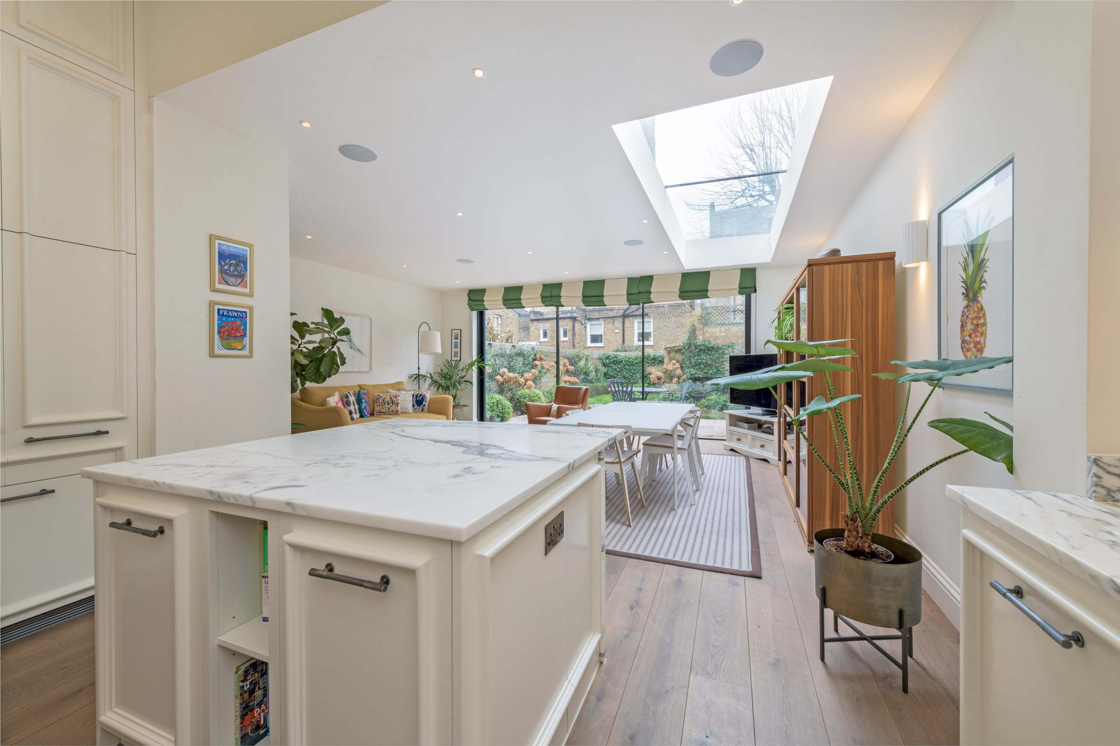 A modern kitchen that opens into a living area, featuring a skylight and sliding doors leading to a garden.