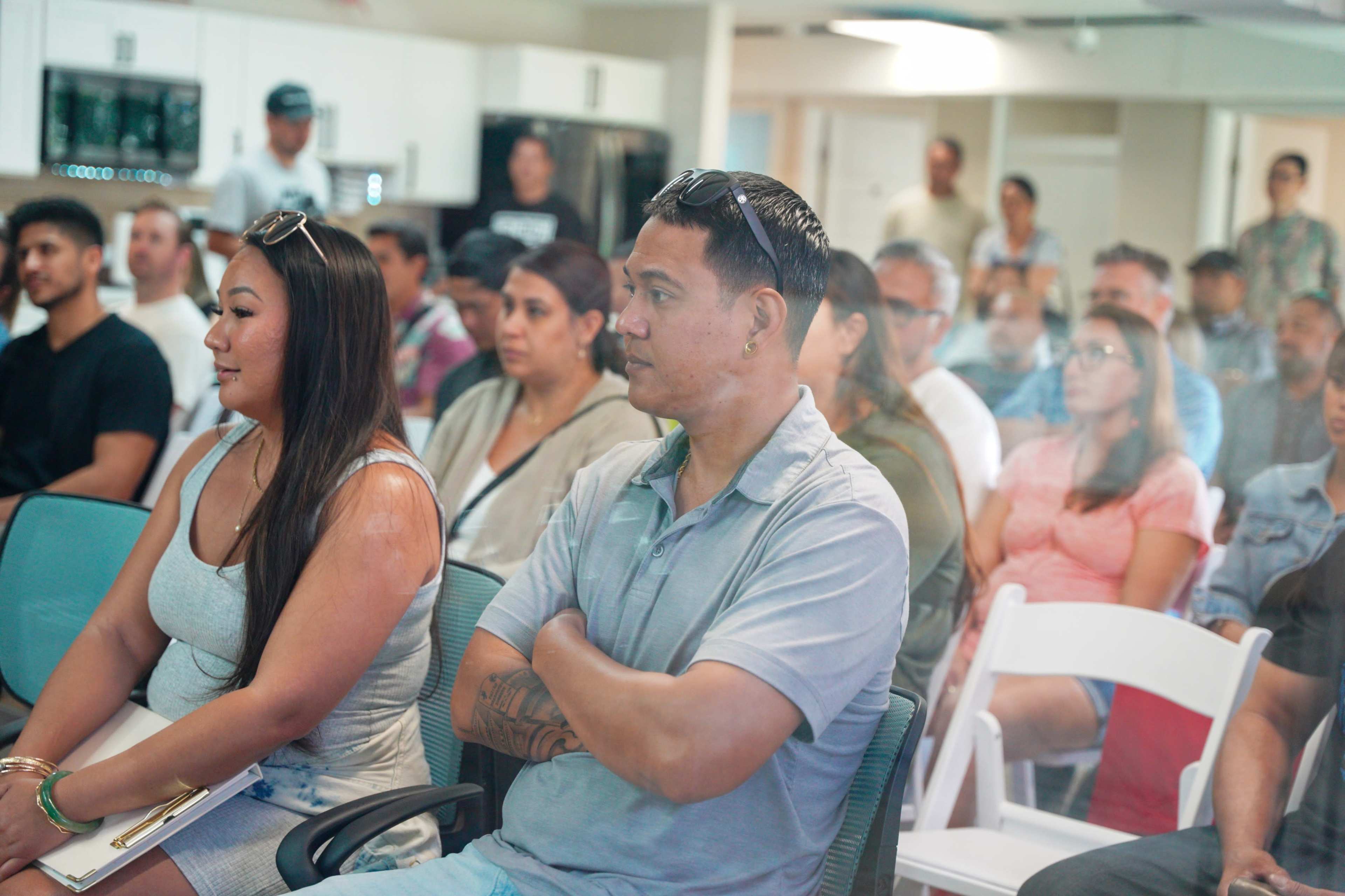 A diverse group of people sits in a modern indoor space, attentively listening to a presentation.