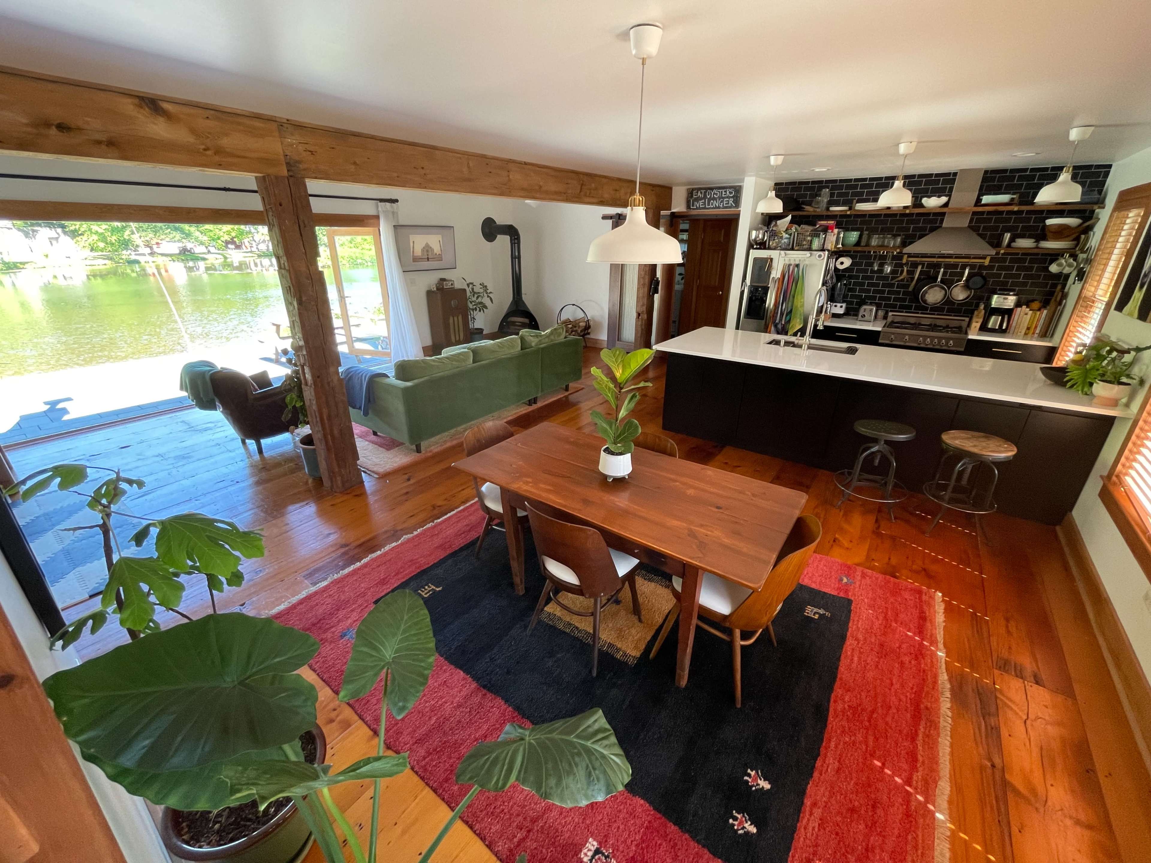 A modern open-concept living area with a dining table, kitchen, and large windows facing a body of water.