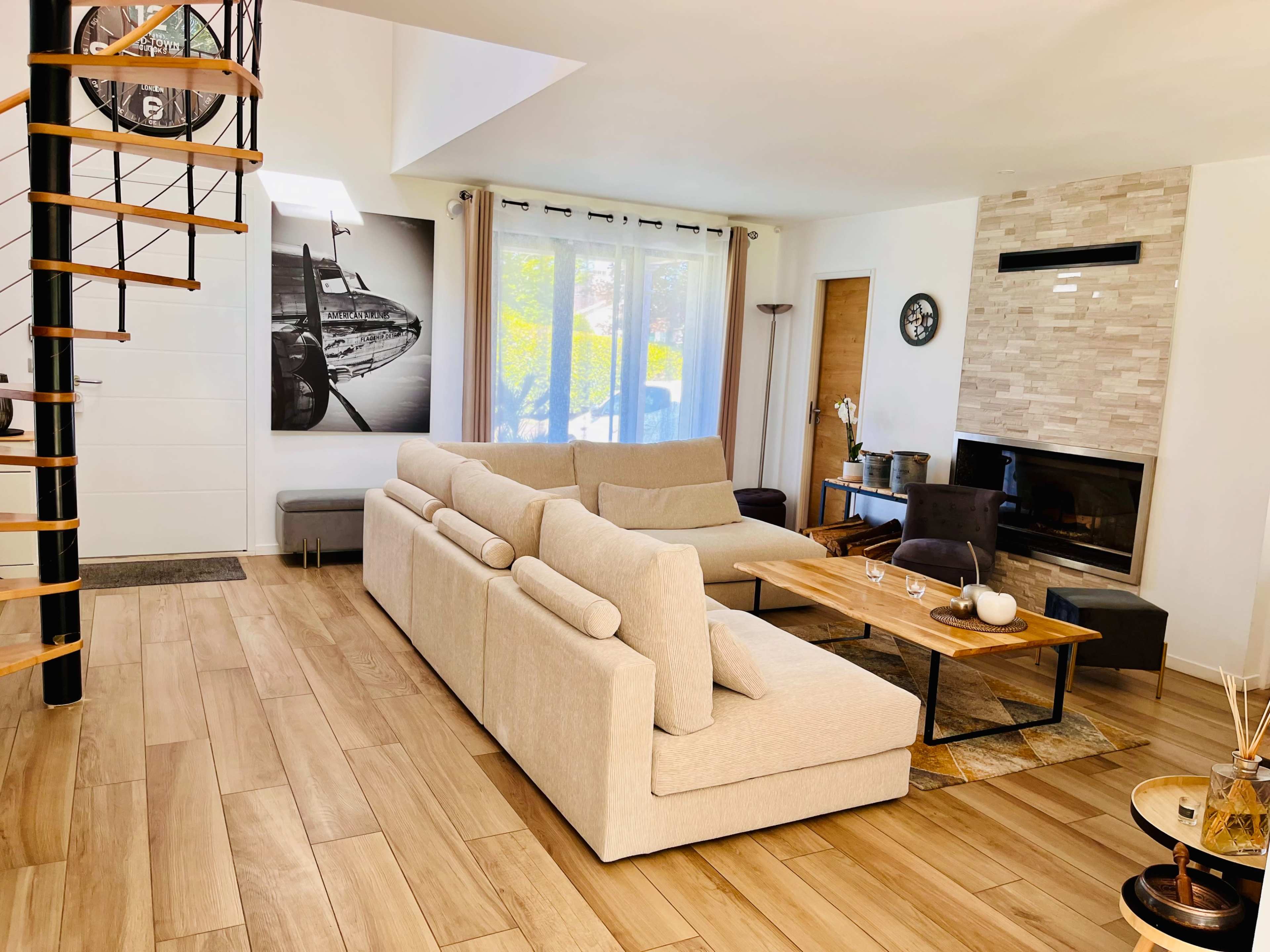 A modern living room with a spiral staircase, a large sectional sofa, a wooden coffee table, and a stone fireplace.