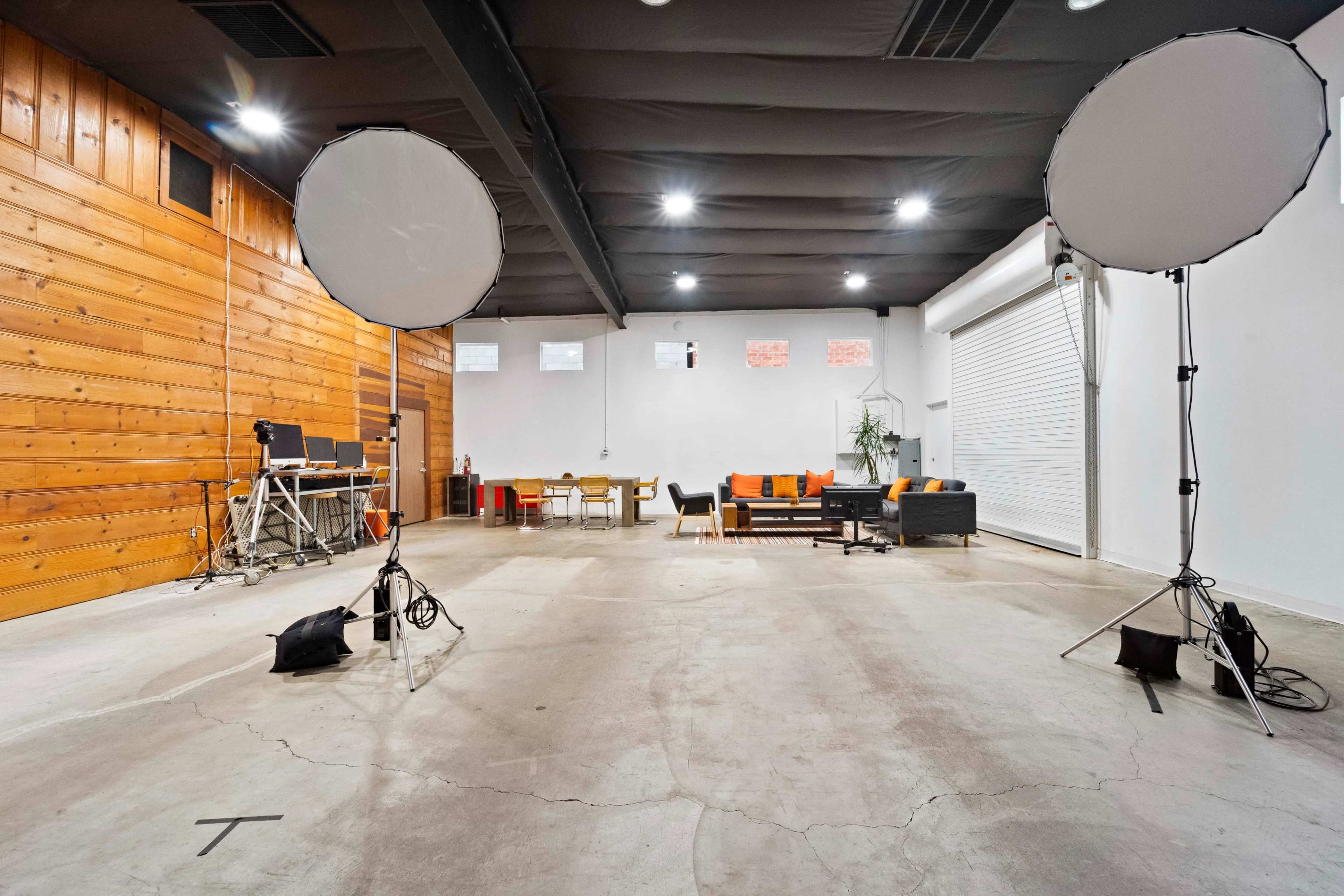 A spacious indoor studio with wooden walls, two large softbox lights, and a seating area with modern furniture.
