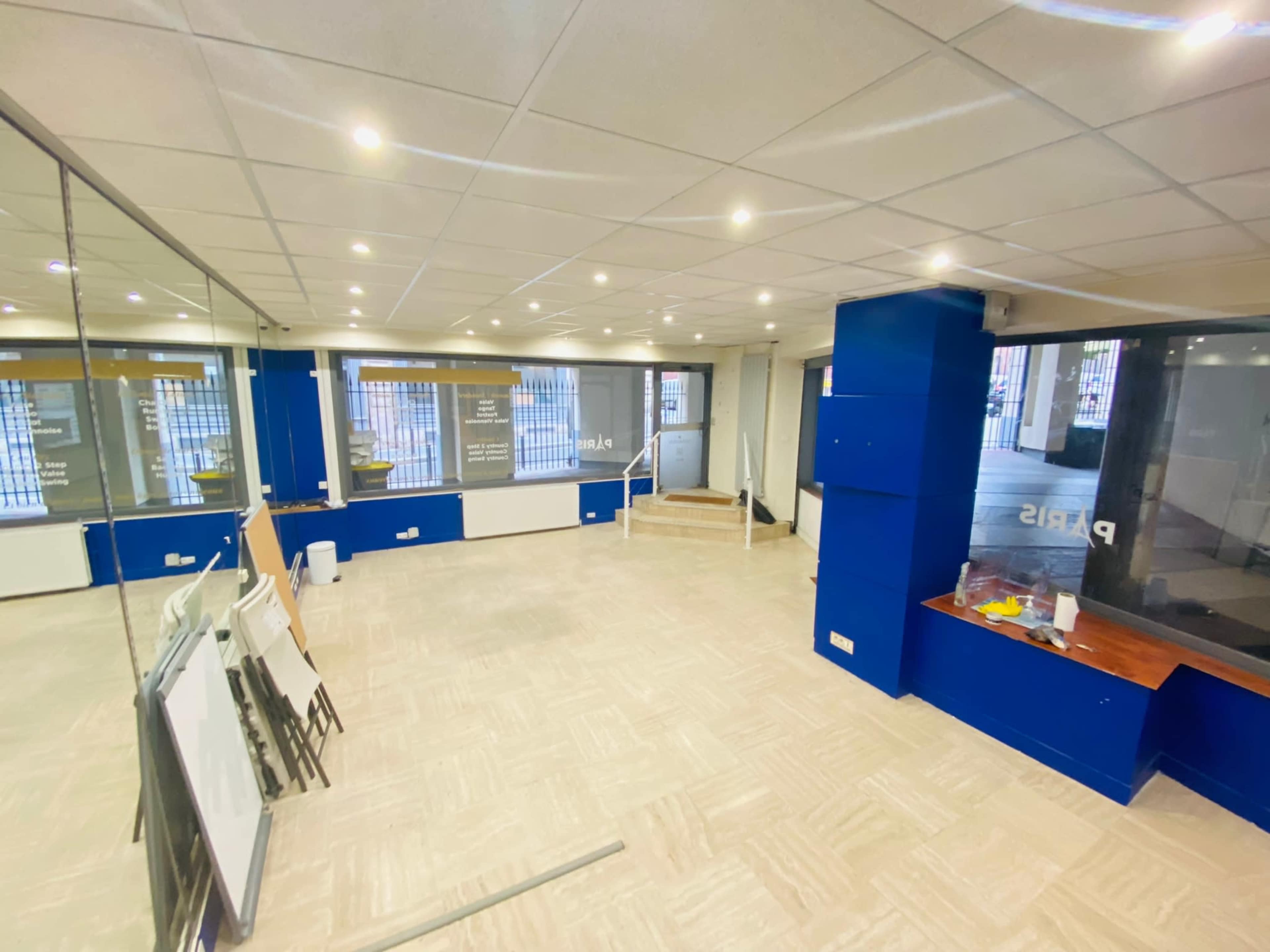 An empty office space with a tiled floor, blue accent walls, and large windows allowing natural light.