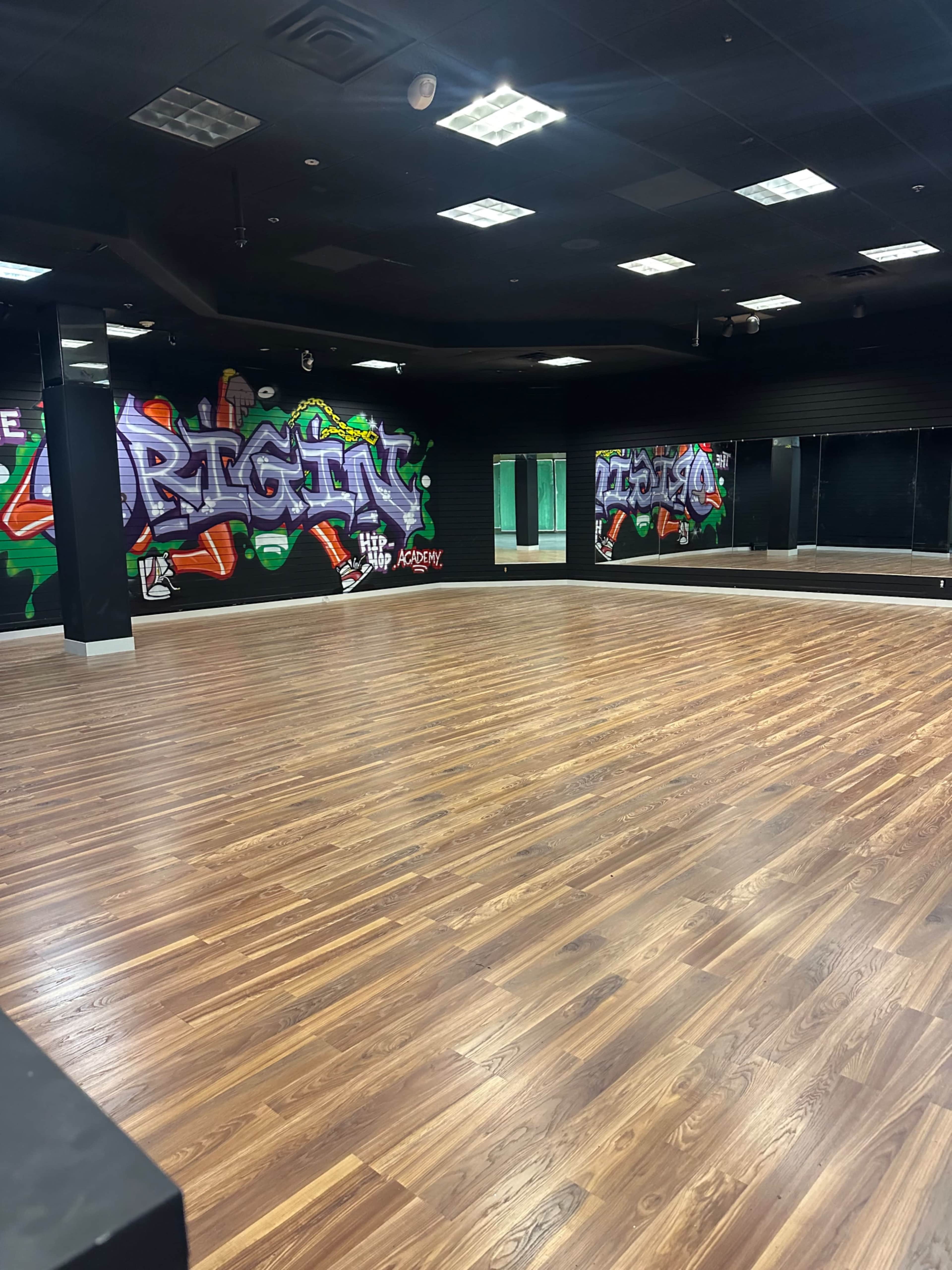 The image shows an empty room with wooden flooring and large mirrors on the walls, featuring colorful graffiti art.