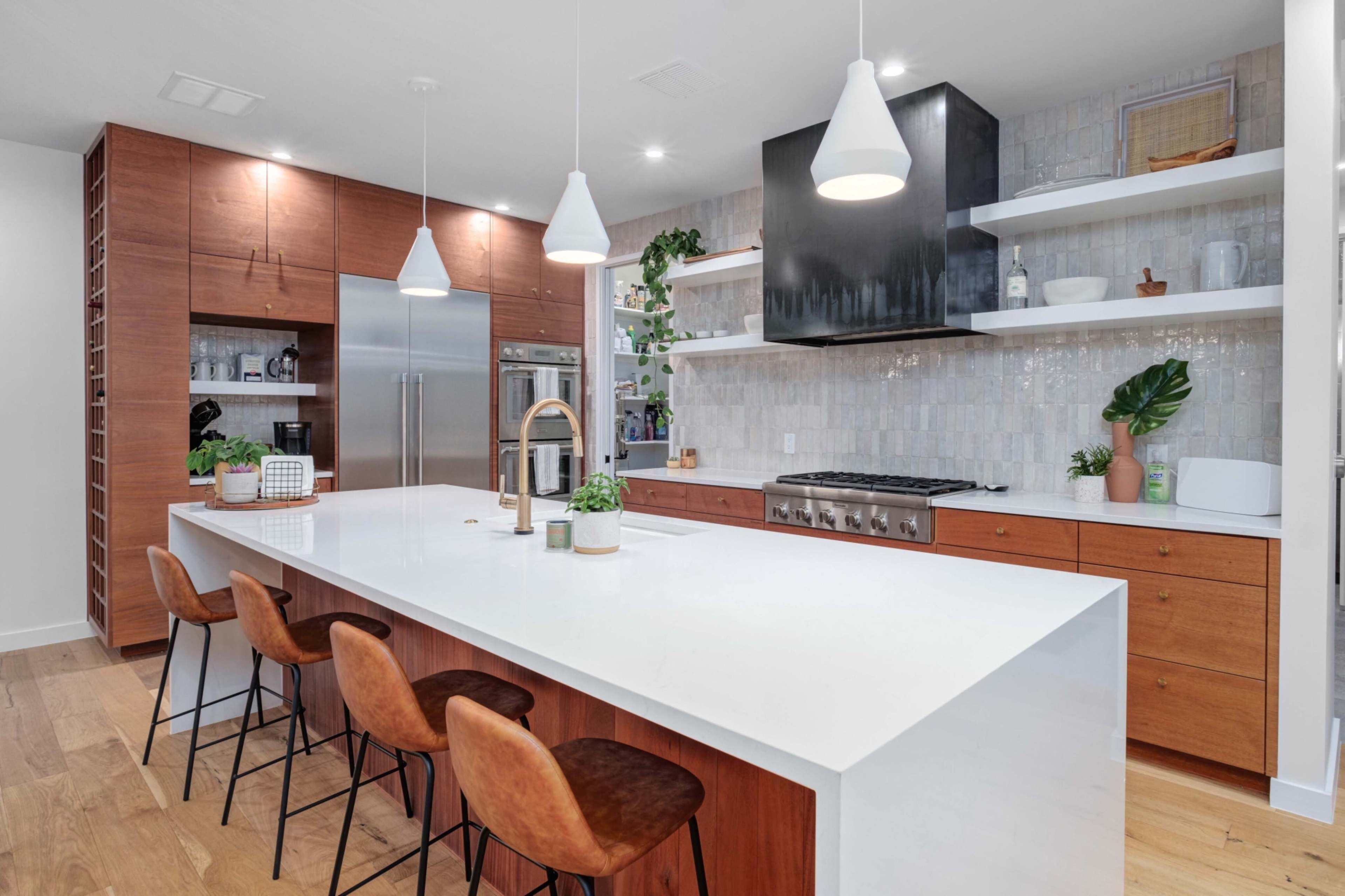 A modern kitchen features a large island with bar seating, stainless steel appliances, and wooden cabinetry.
