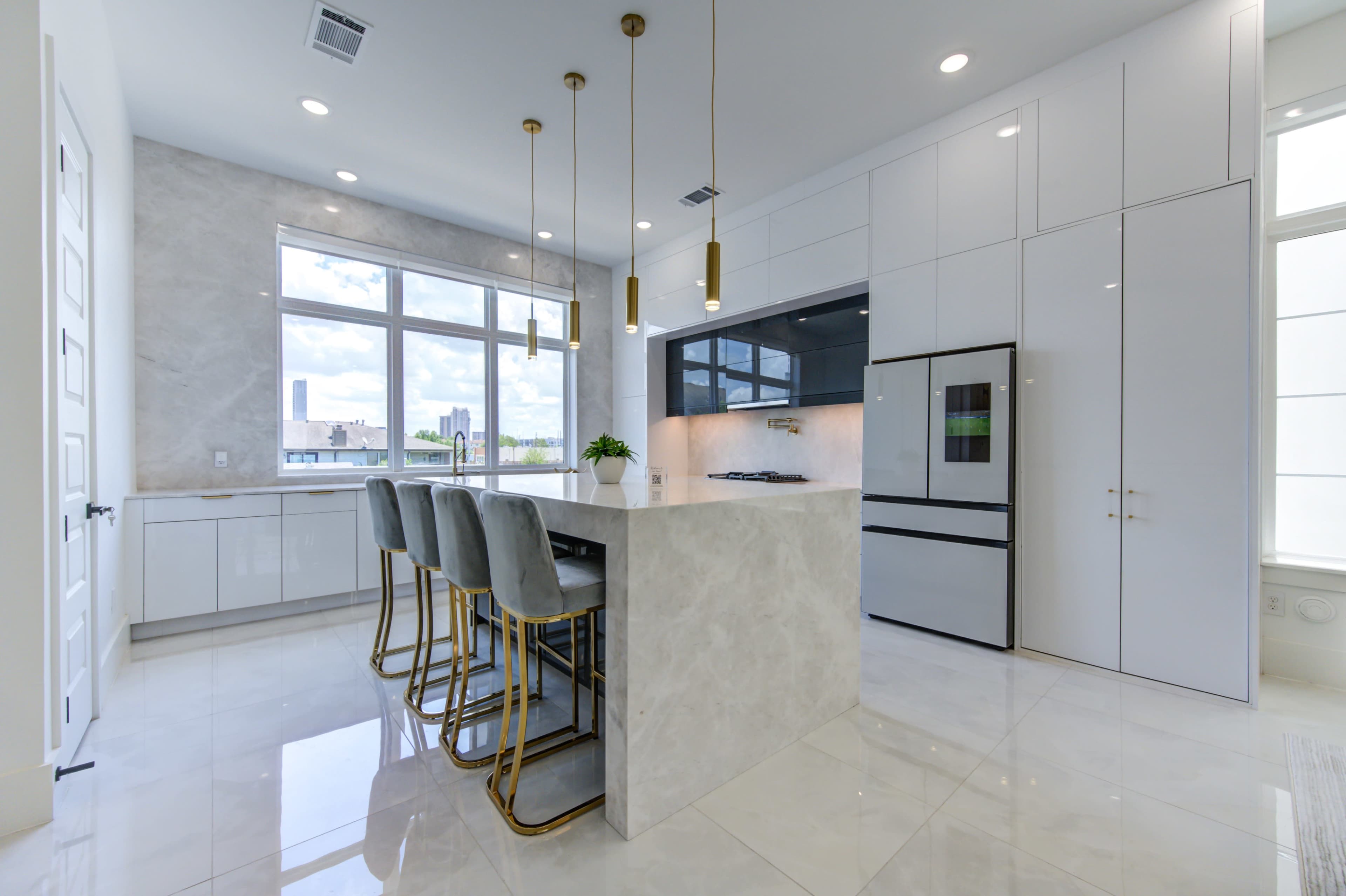 A modern kitchen features a large island with seating, sleek cabinets, and large windows allowing natural light.