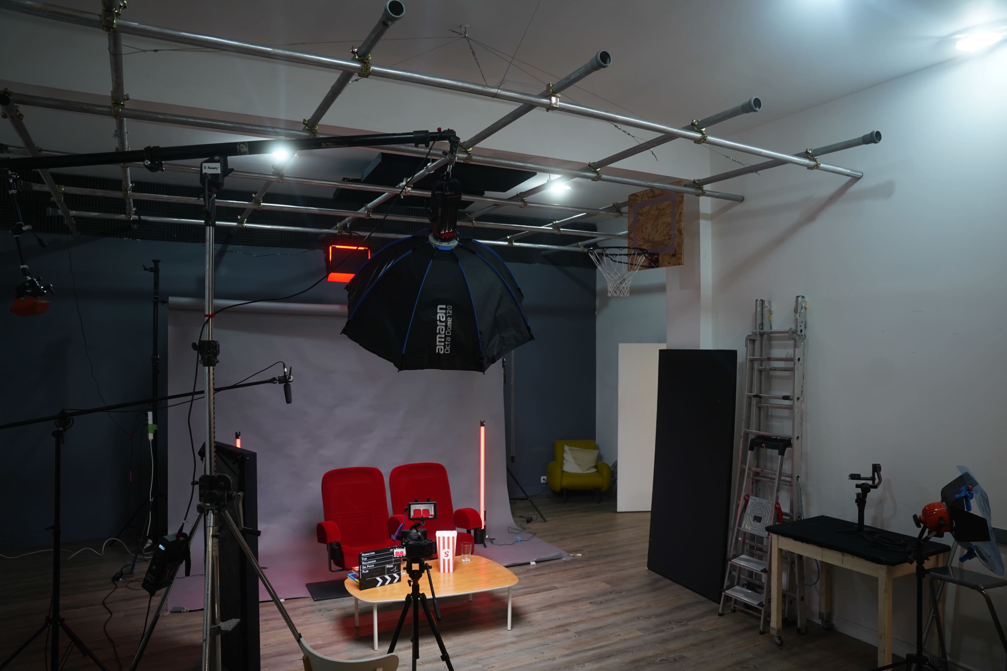 The image shows a photography studio setup with red chairs, a backdrop, lighting equipment, and a basketball hoop in the background.