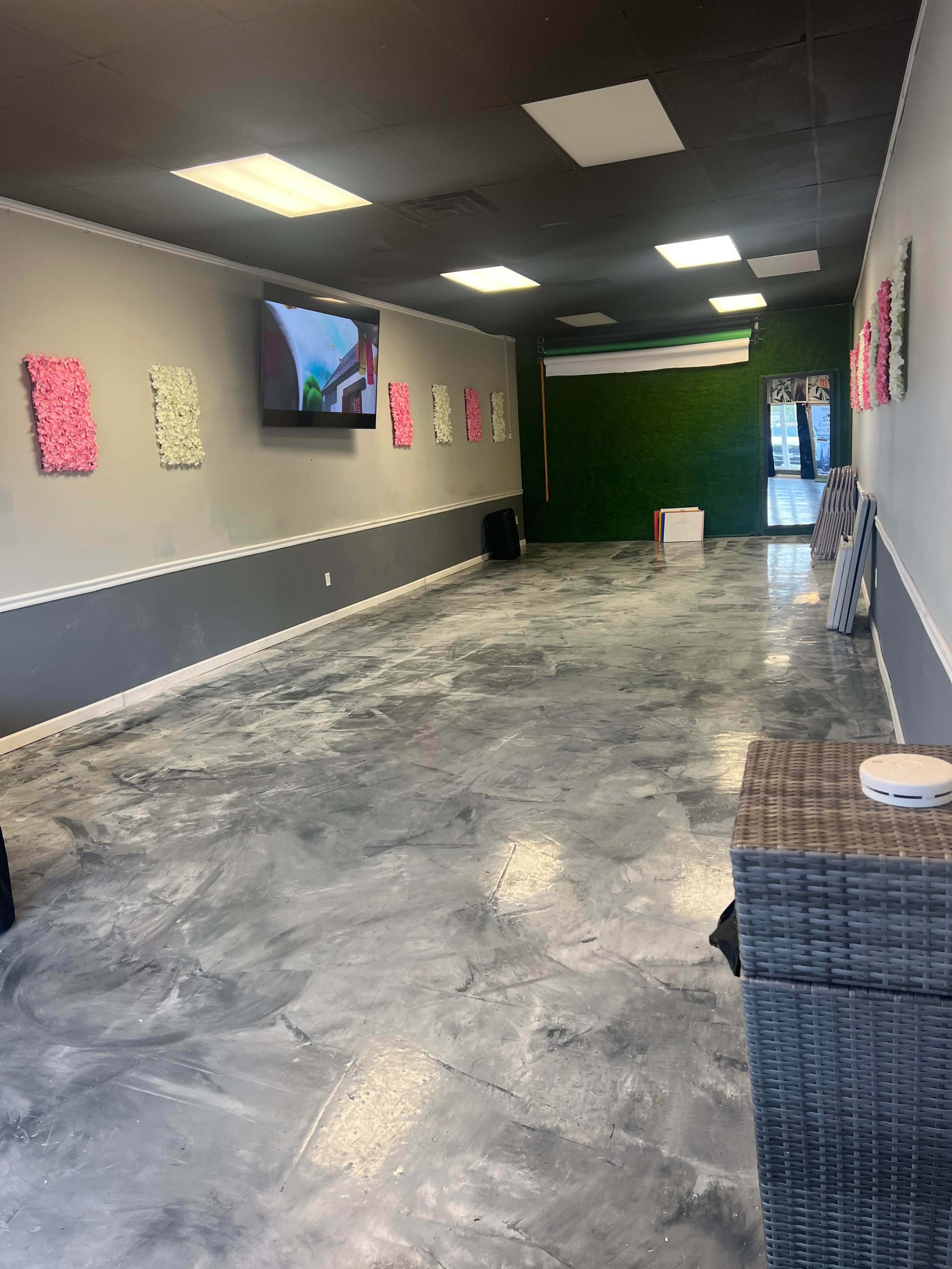 An empty indoor space with gray walls, a polished floor reflecting light, and decorative elements on the walls, including TV and floral art.
