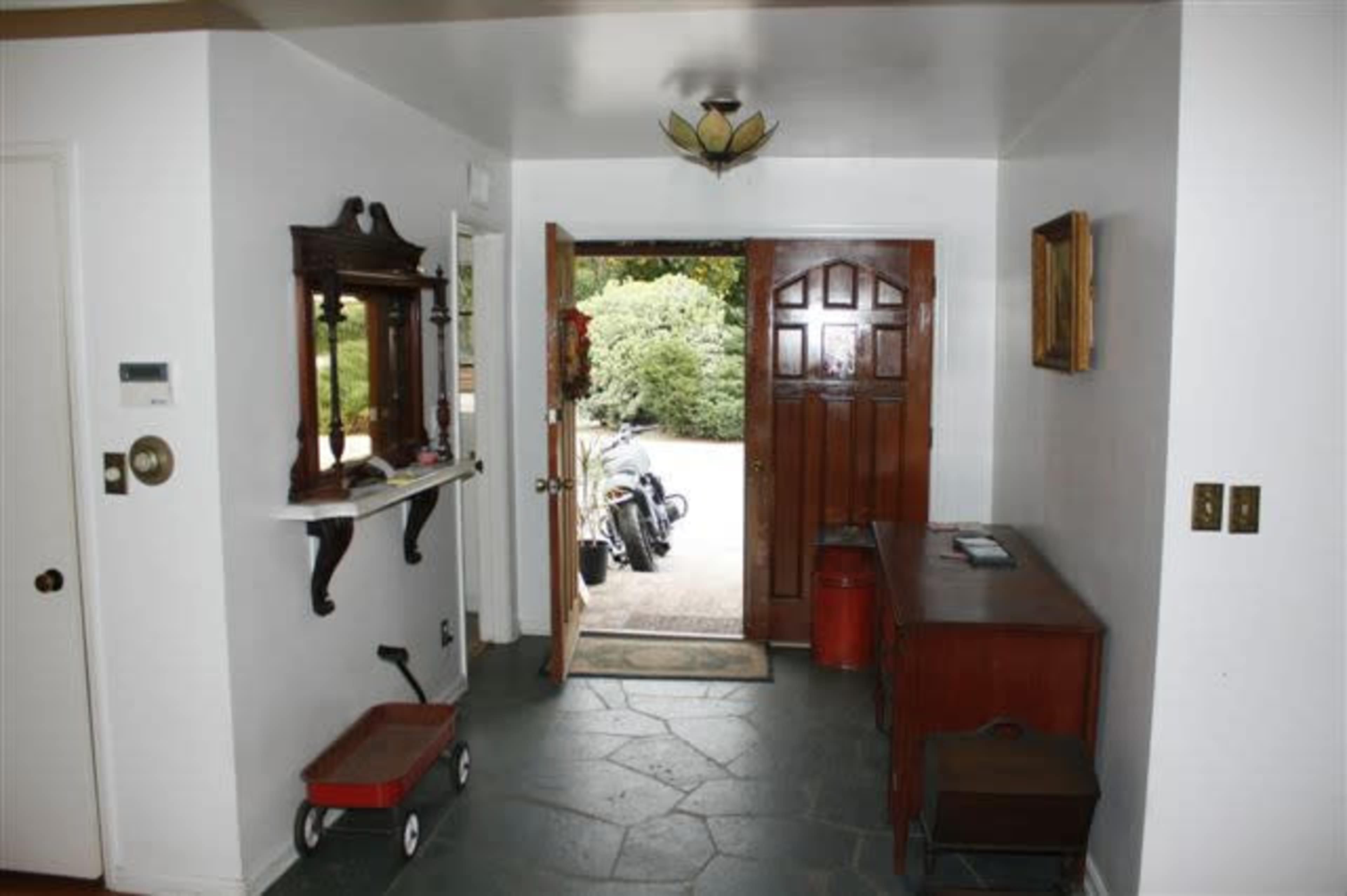 A foyer with a wooden door leading outside, a coat rack, a table against the wall, and a glimpse of a motorcycle parked outside.