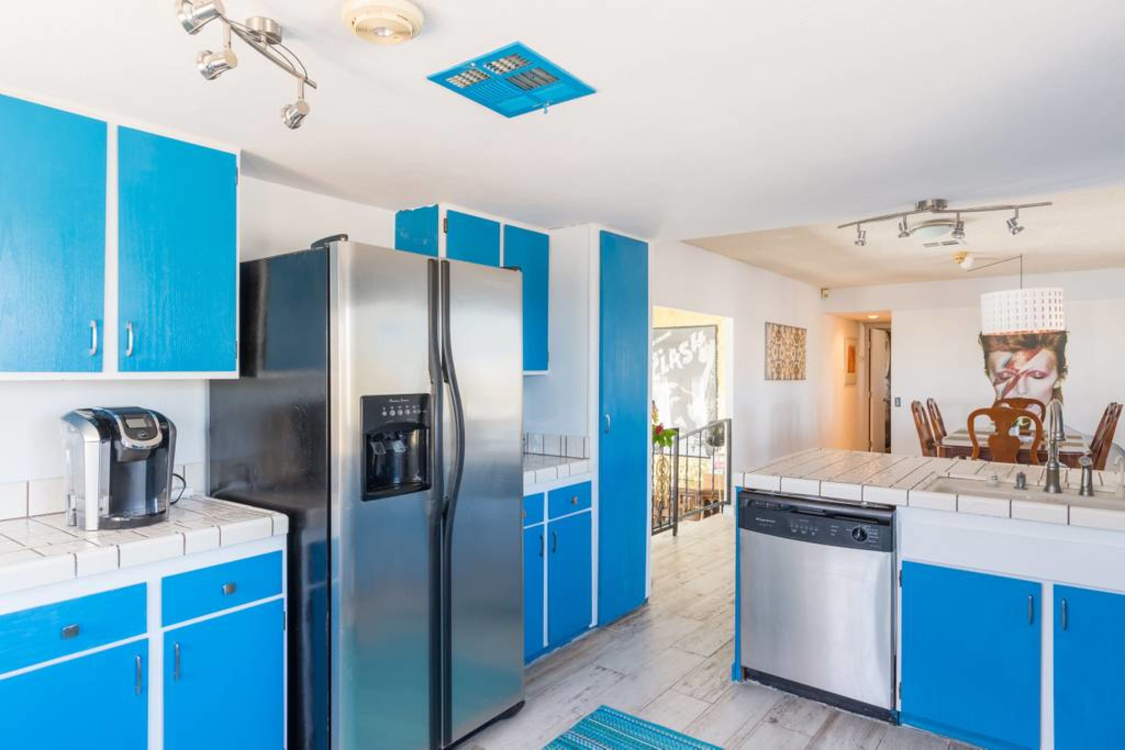 A kitchen with blue cabinets, a stainless steel refrigerator, and a white tiled countertop.