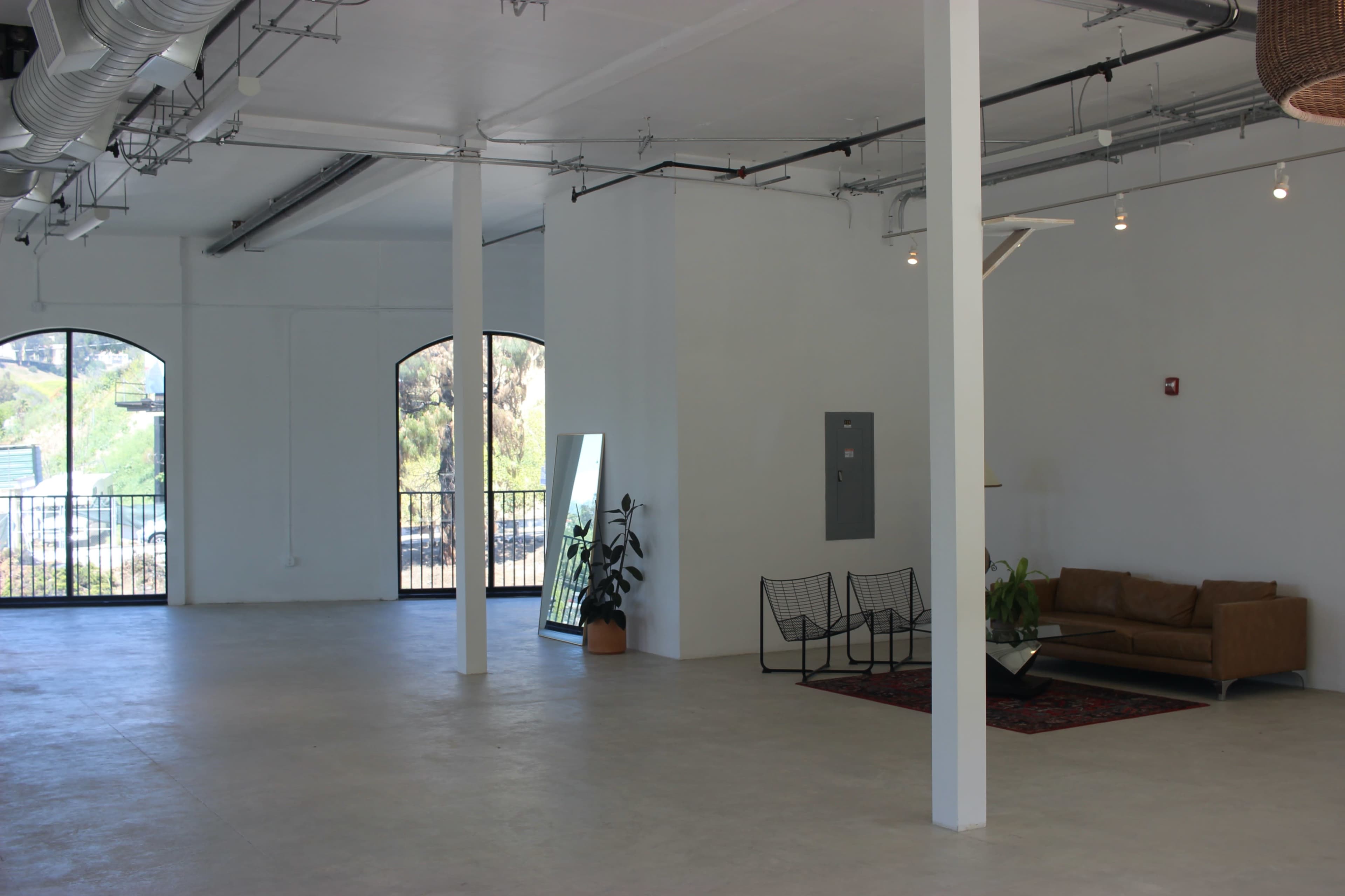 A spacious, empty interior with large windows, a sofa, and chairs arranged on a rug.