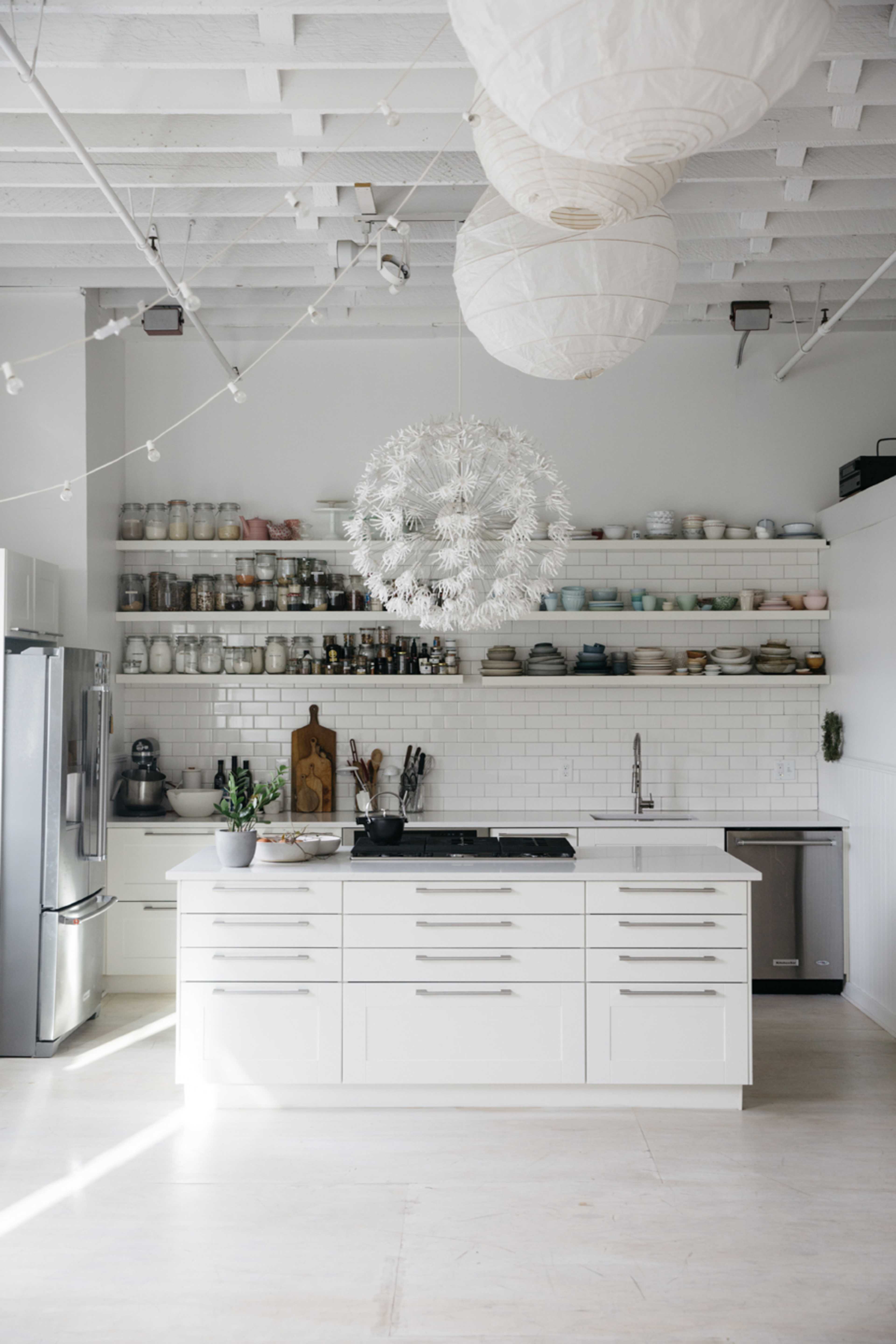 A modern kitchen features white cabinetry, open shelving with dishware, a central island with a cooktop, and pendant lighting.