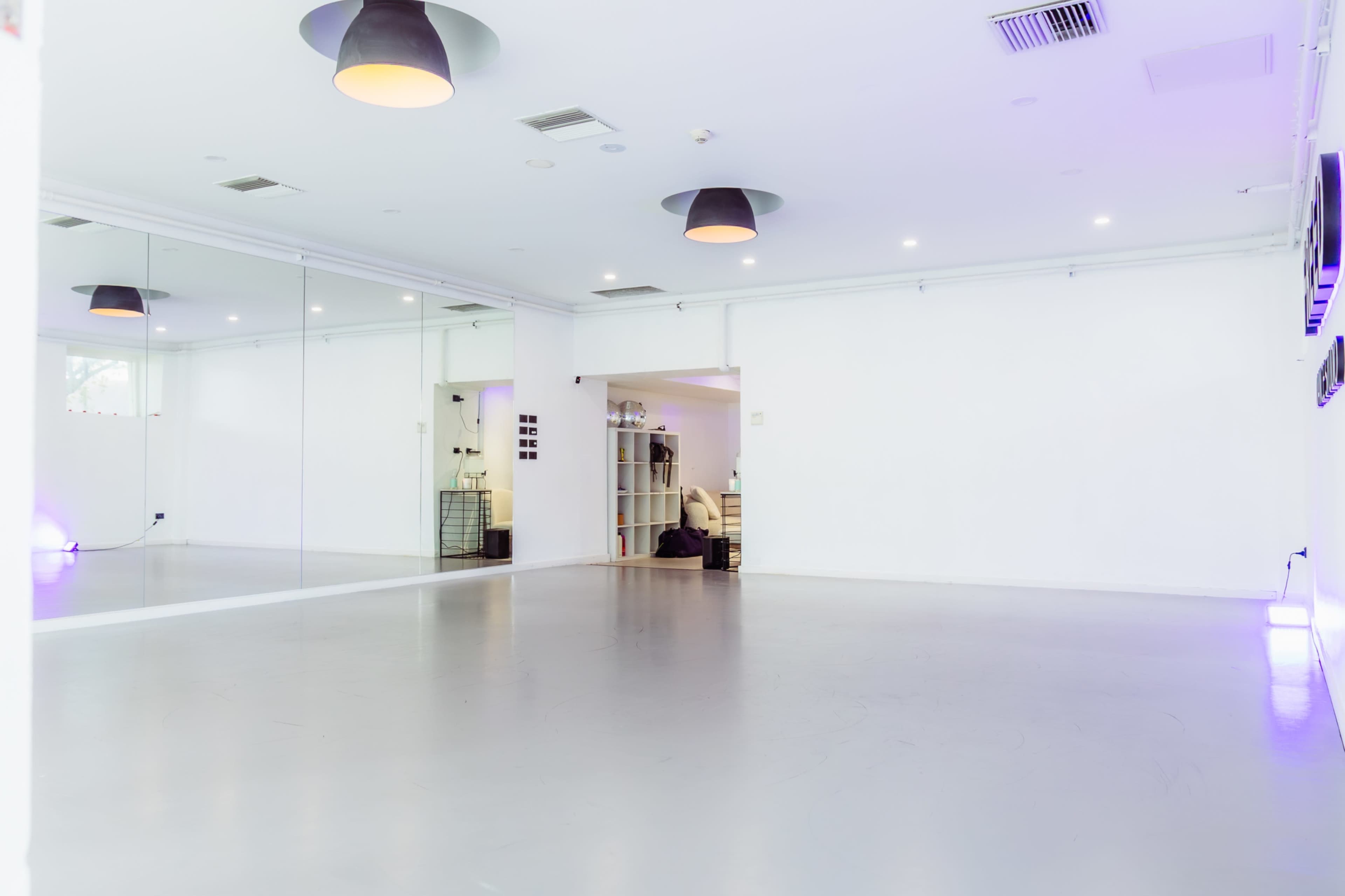 The image shows a bright, empty studio space with large mirrors on one wall and minimal furnishings in the background.