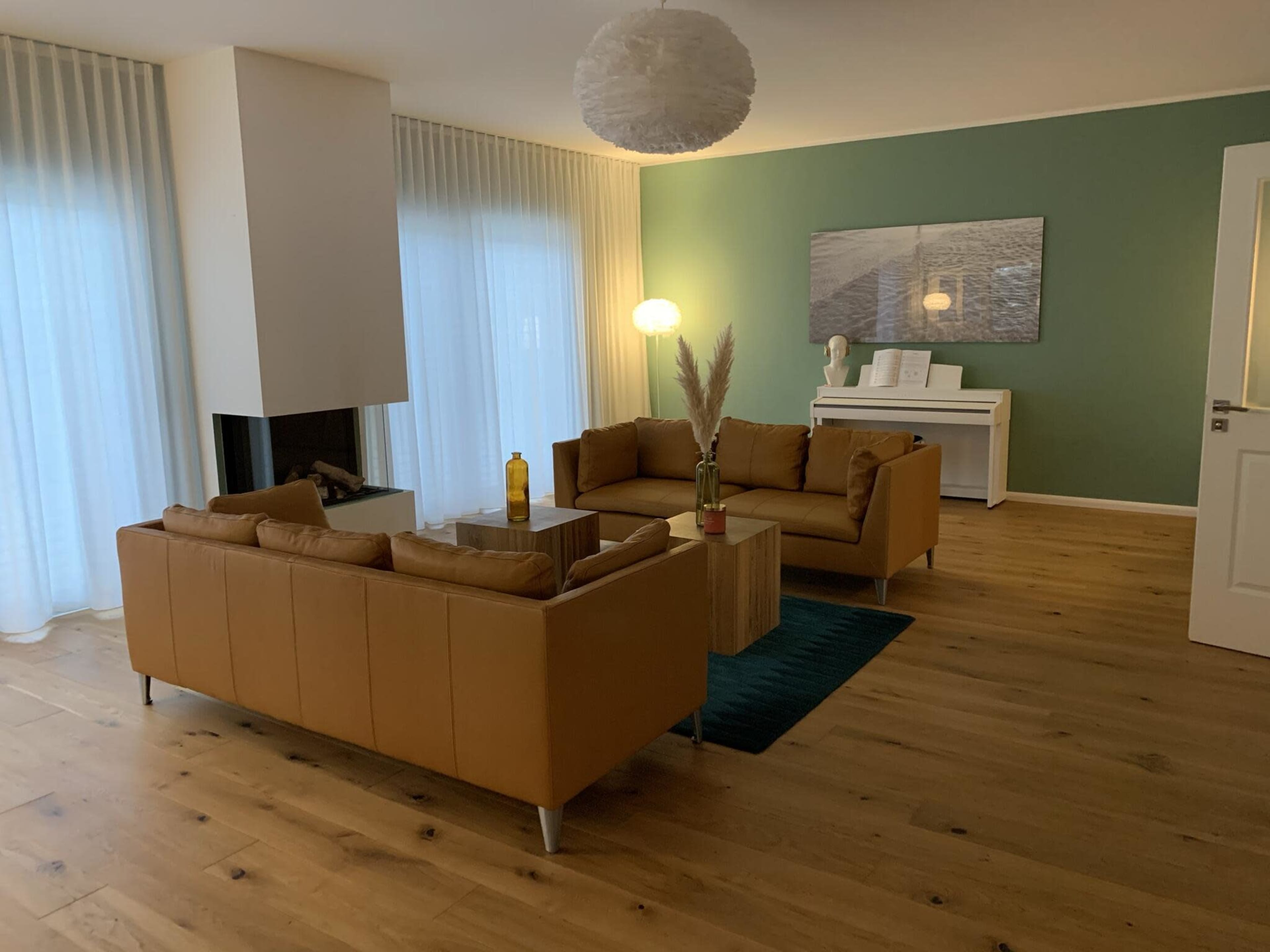 A modern living room featuring two tan leather sofas around a wooden coffee table, with a fireplace and a piano in the background.