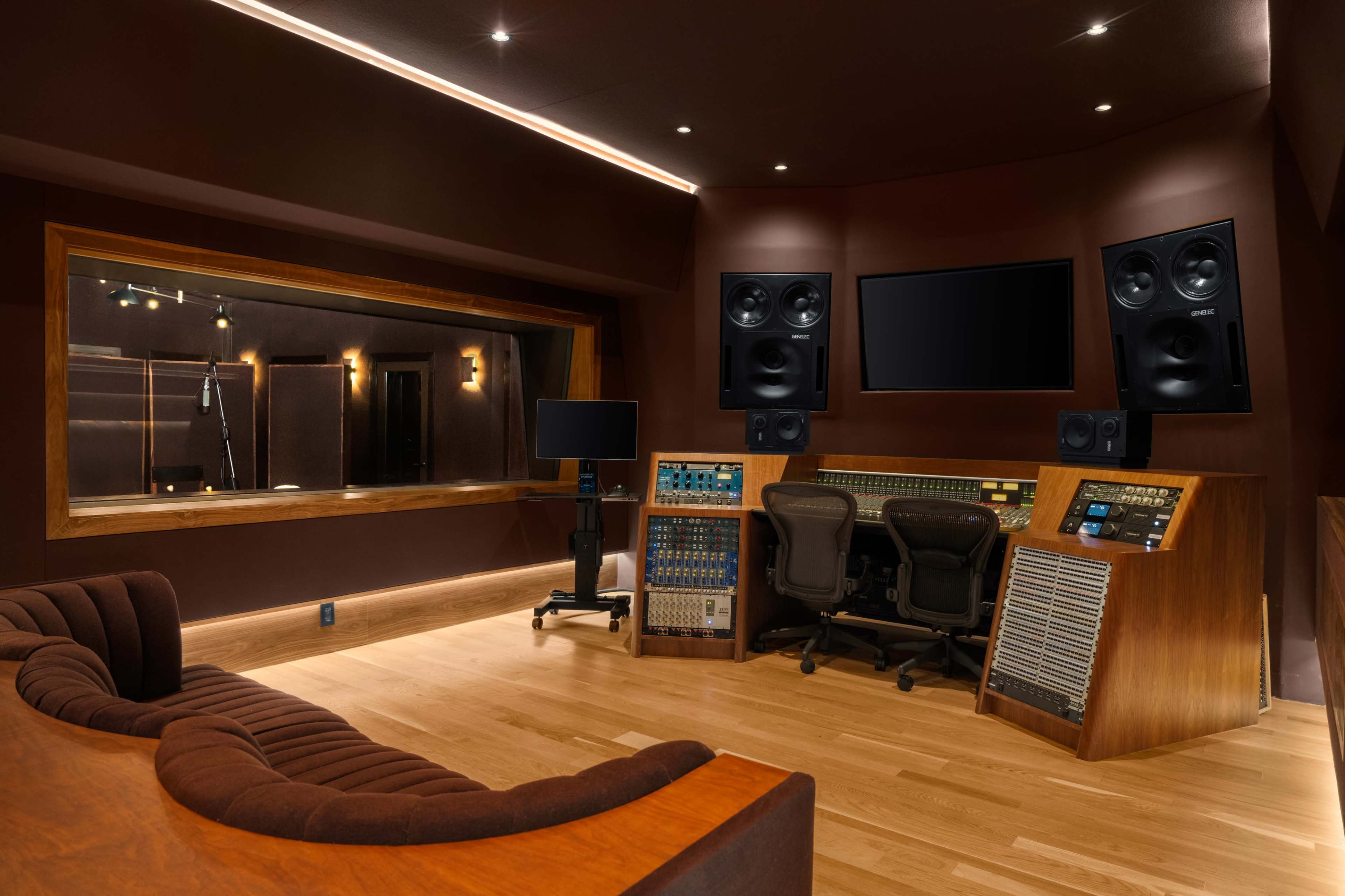 The image shows a modern audio recording studio with a control desk, speakers, and a glass booth for vocal recording.
