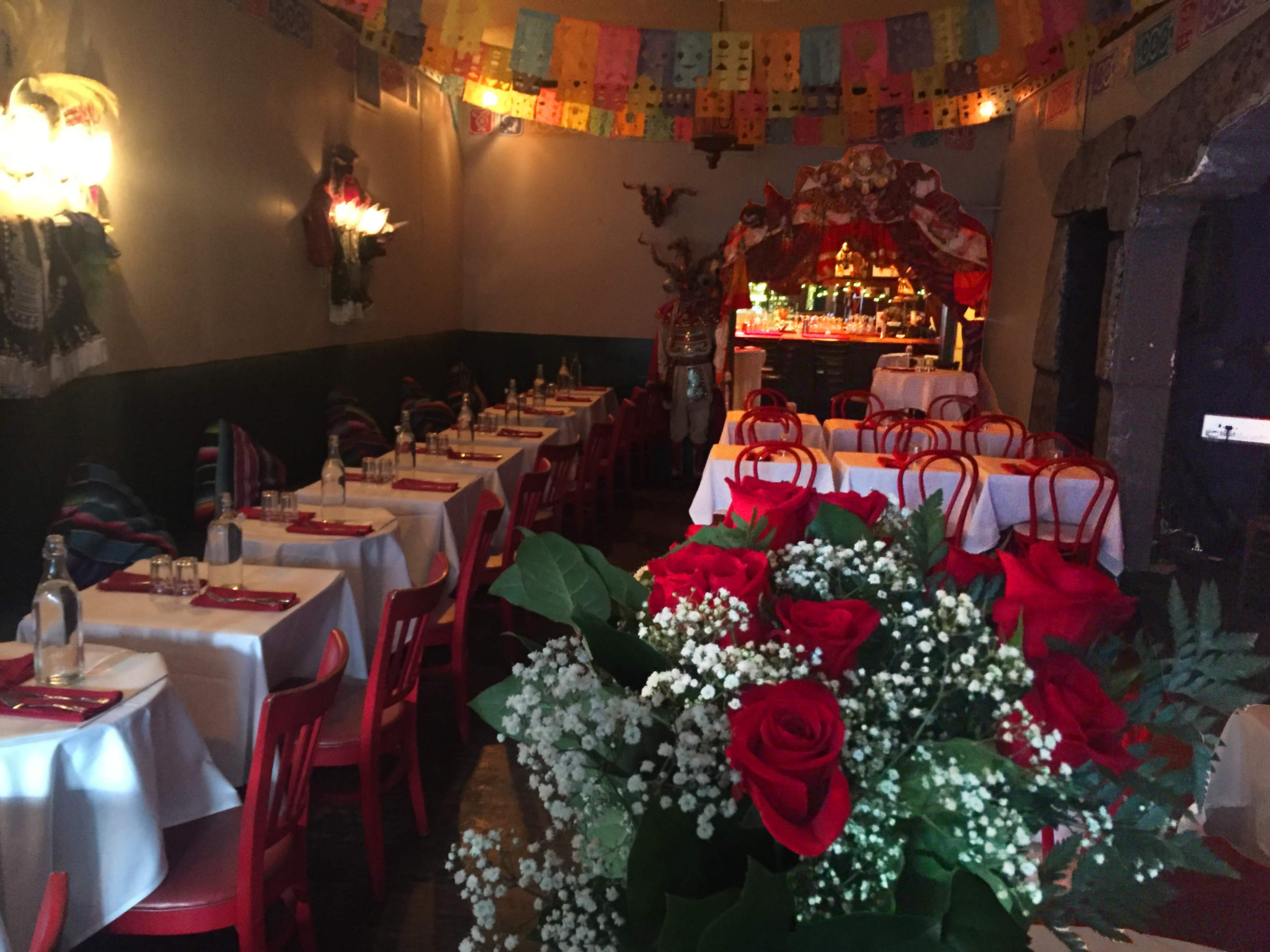 The image shows a colorful restaurant interior featuring red chairs, white tablecloths, and festive decorations with paper banners hanging from the ceiling.