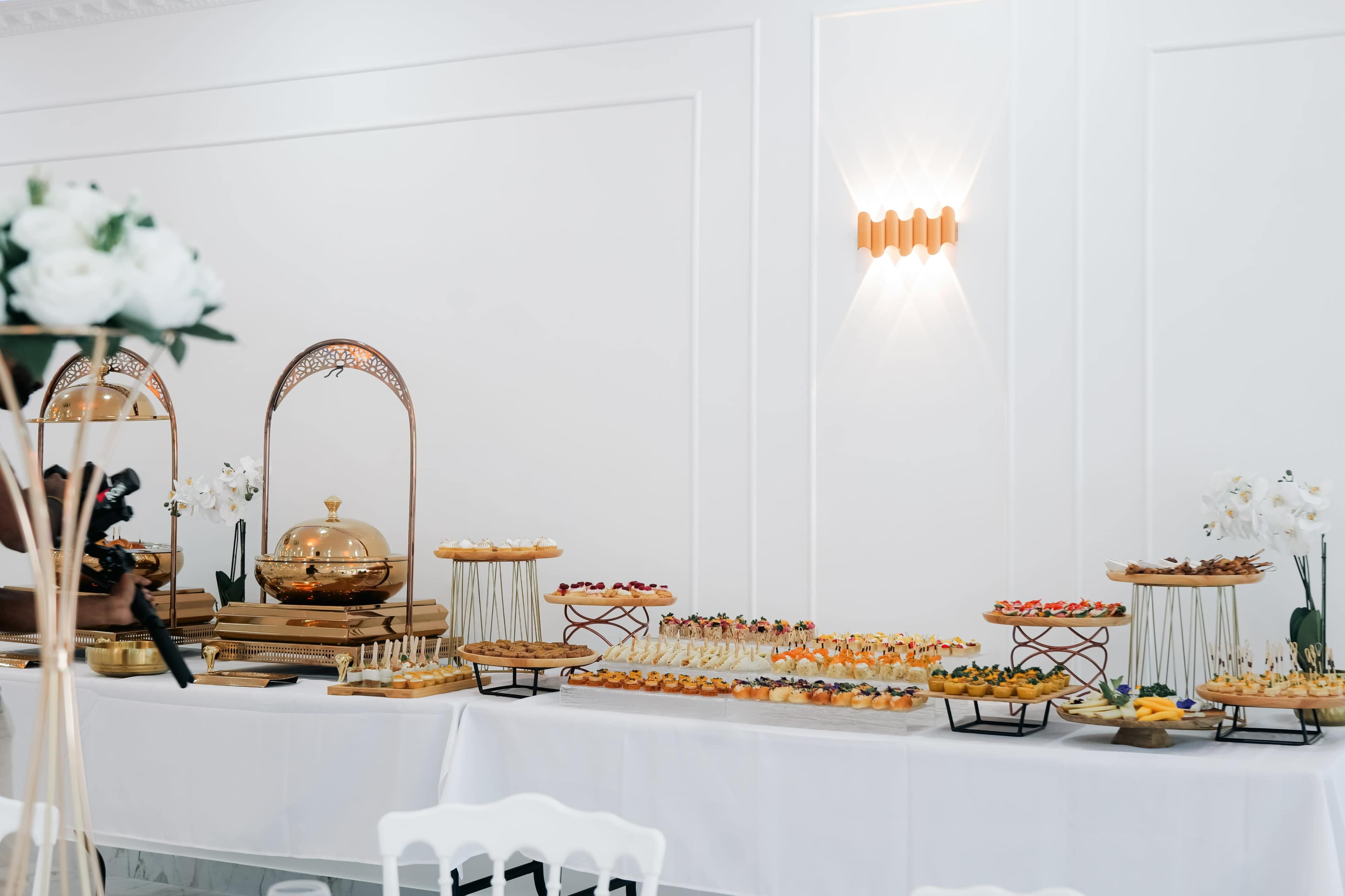 A long table displays an assortment of elegant hors d'oeuvres and desserts in a well-lit event space.
