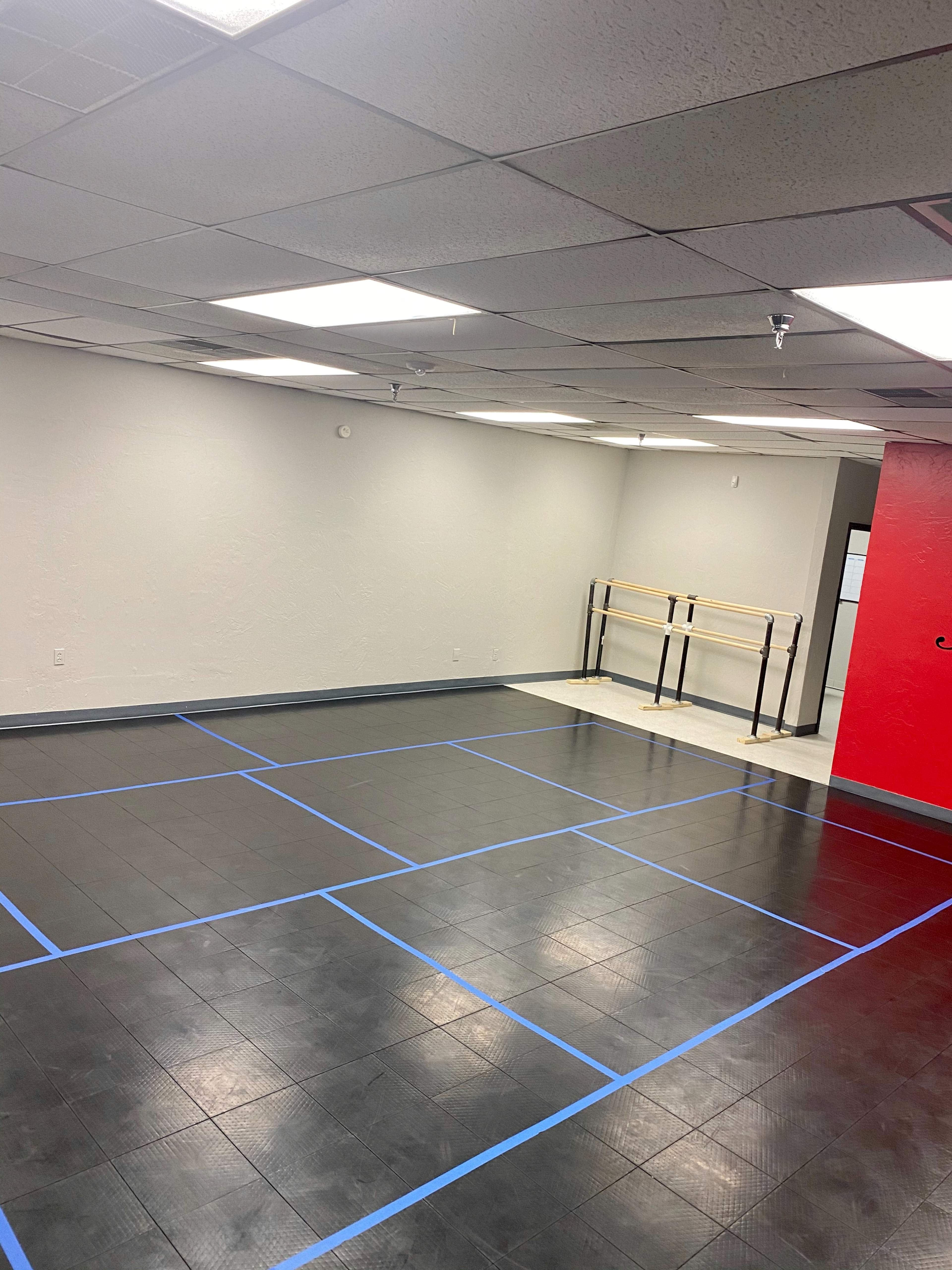 A spacious empty room with blue tape marking a dance floor layout and a red wall on one side.