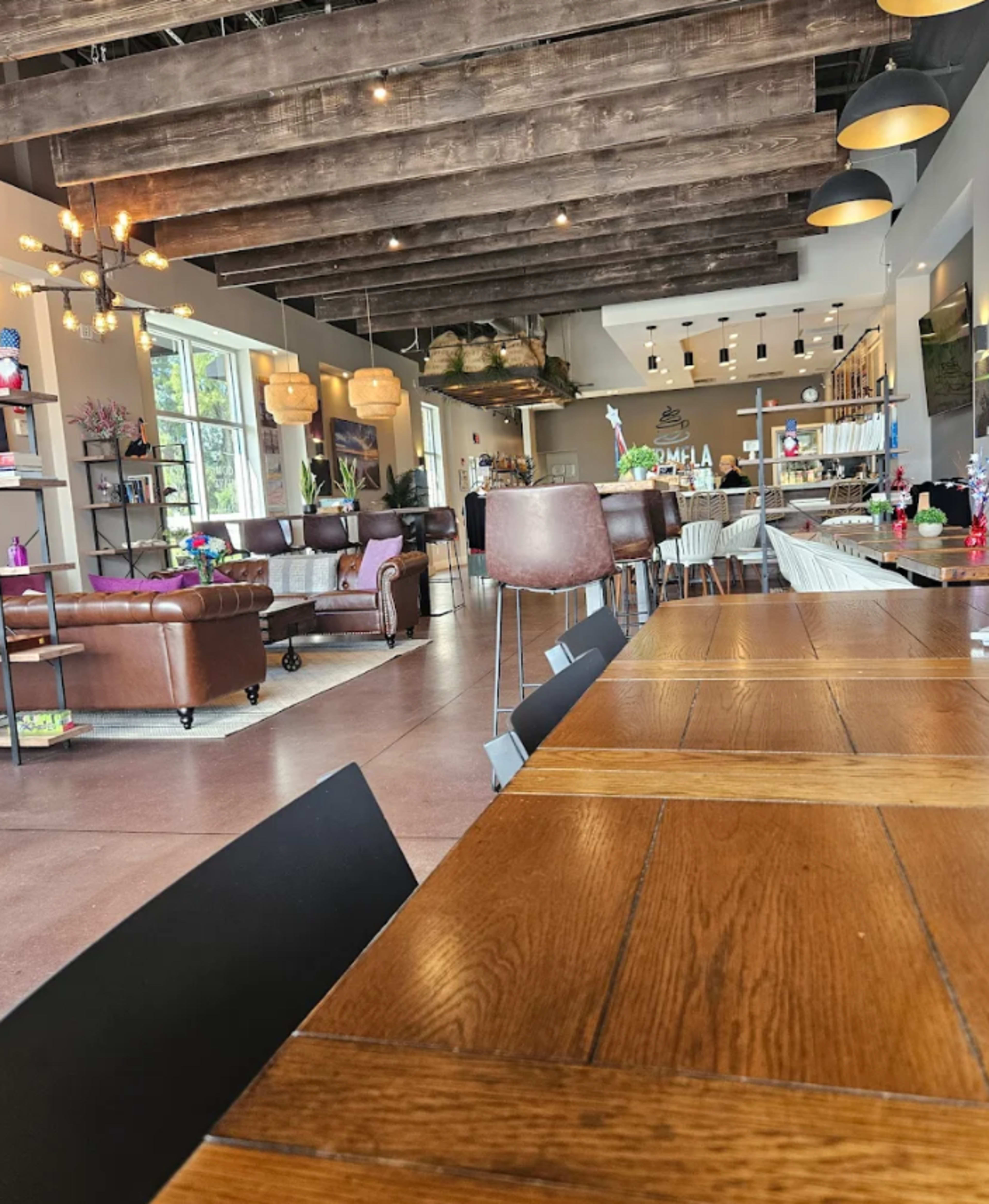 The image shows a spacious cafe with wooden beams, comfortable seating areas, and a variety of decorative elements.
