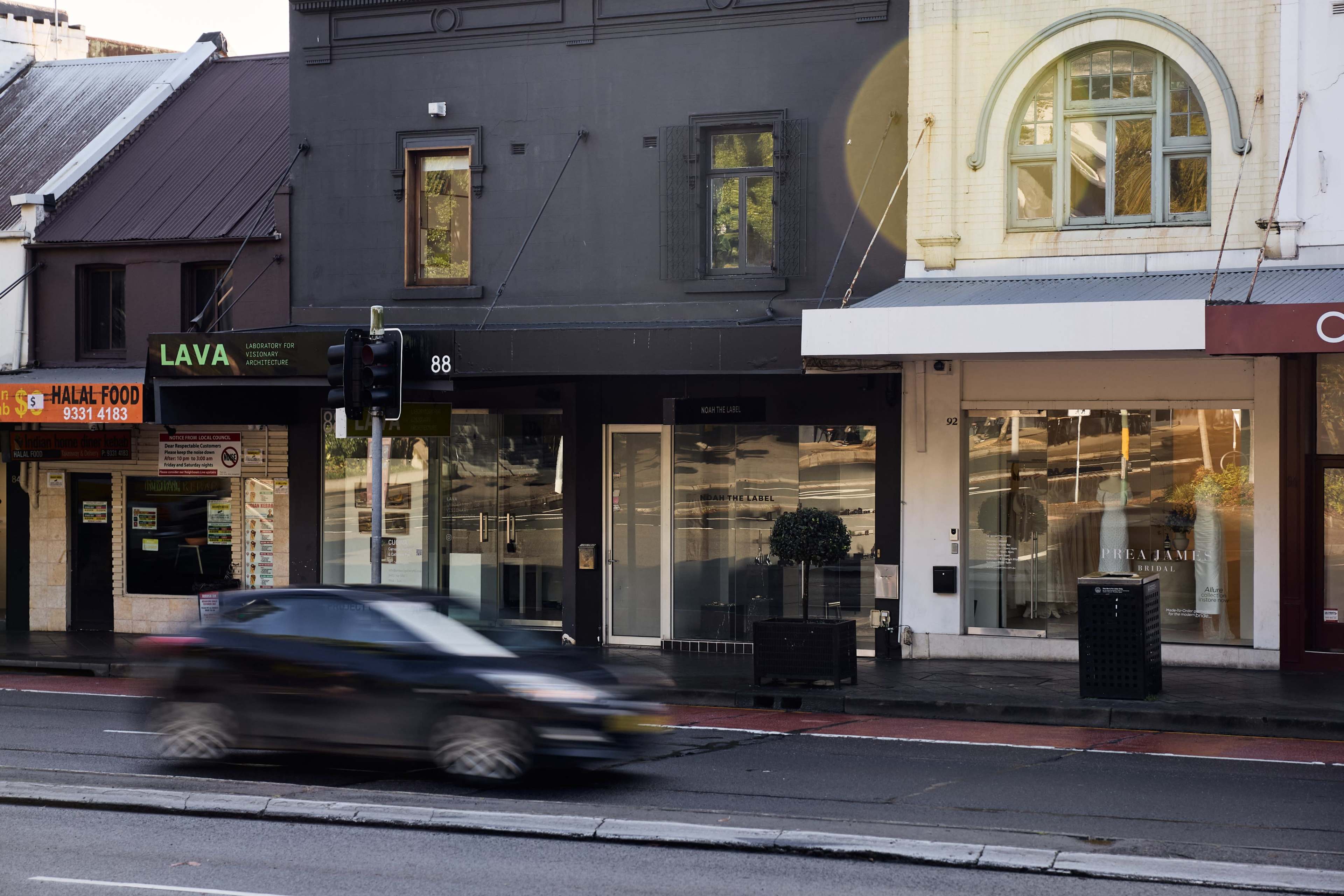 The image features a street view with a moving car in front of several shops, including a business labeled "LAVA," and a storefront with large glass windows.