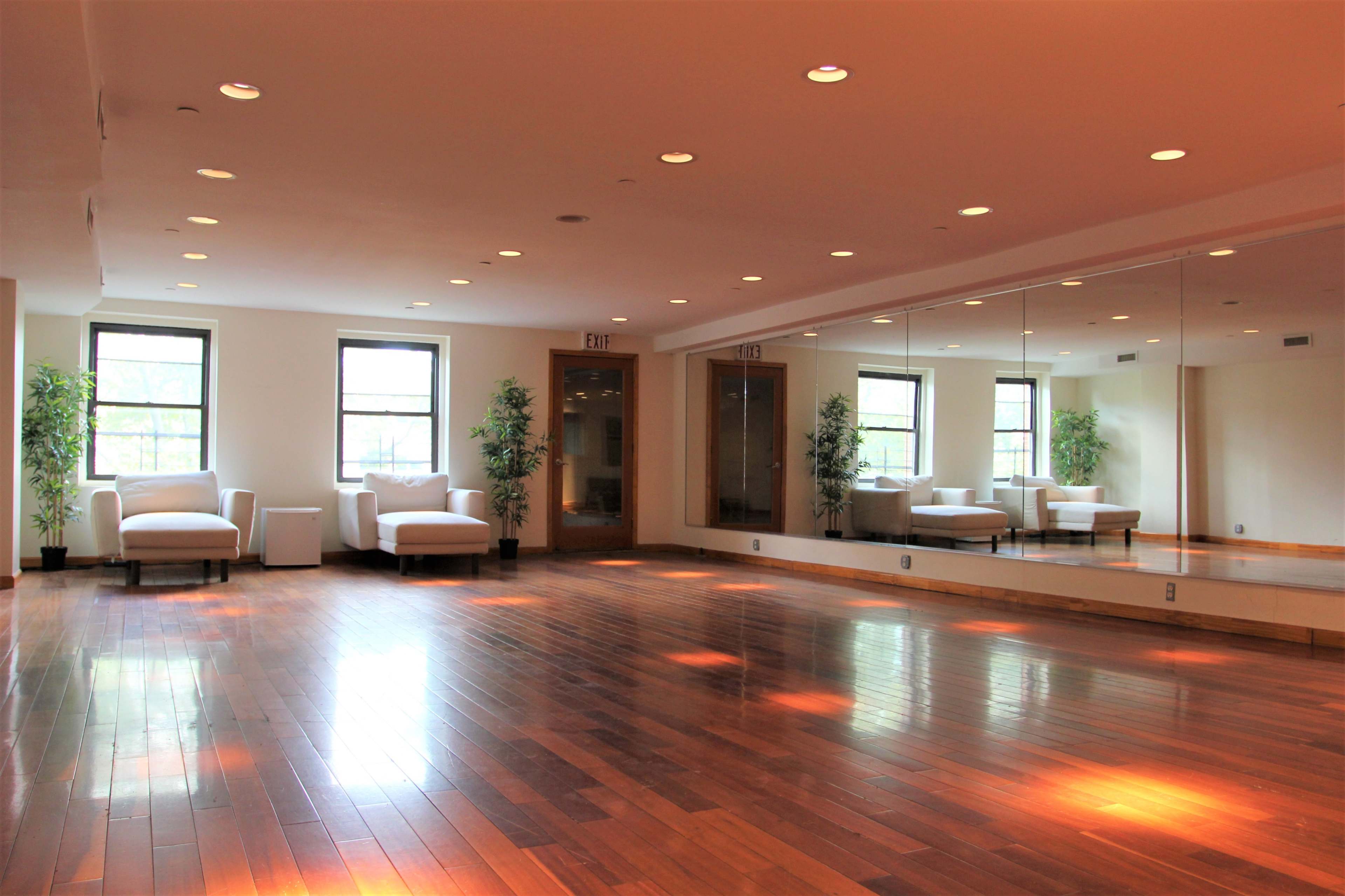 A spacious room with hardwood floors, two white chairs, and large mirrors along one wall.