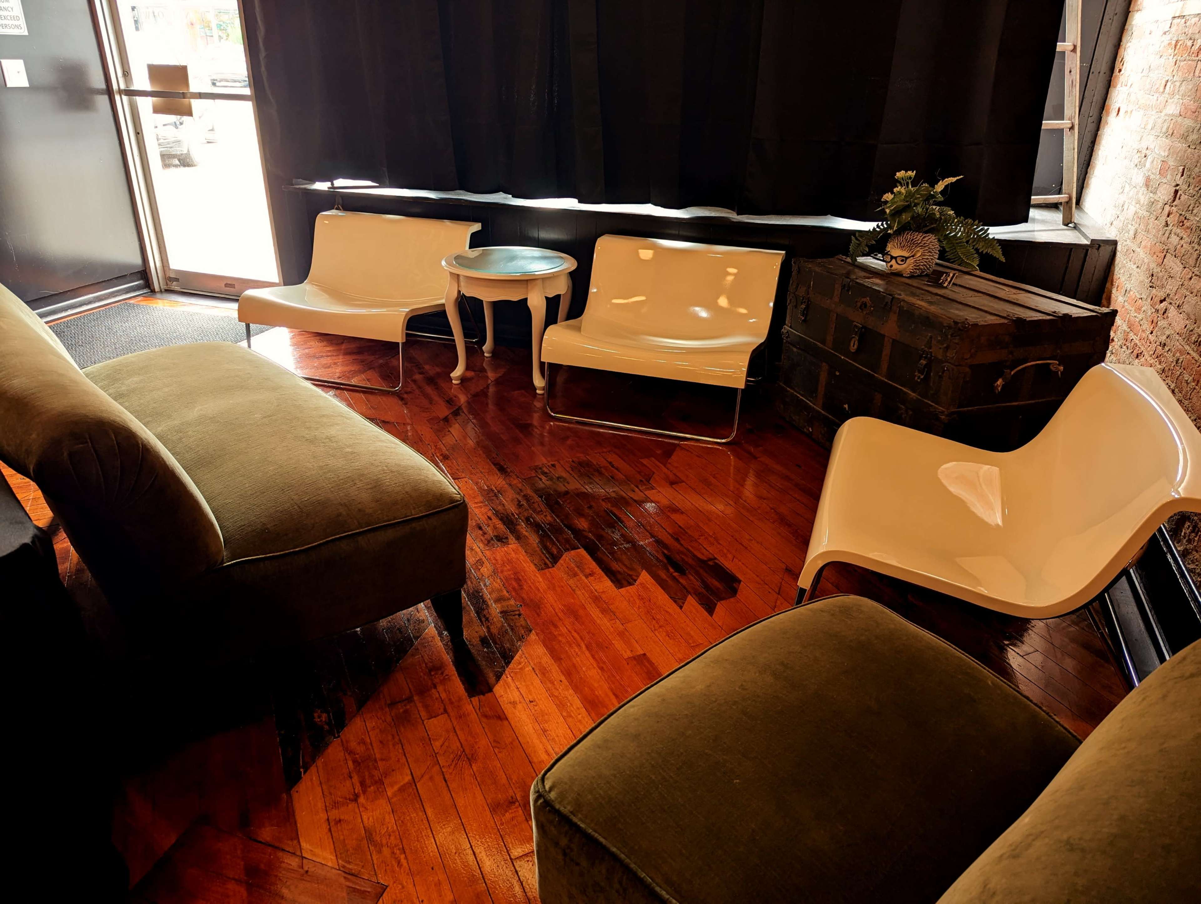 A small lounge area with two green sofas and two white chairs around a small blue table, situated near a window with black curtains.