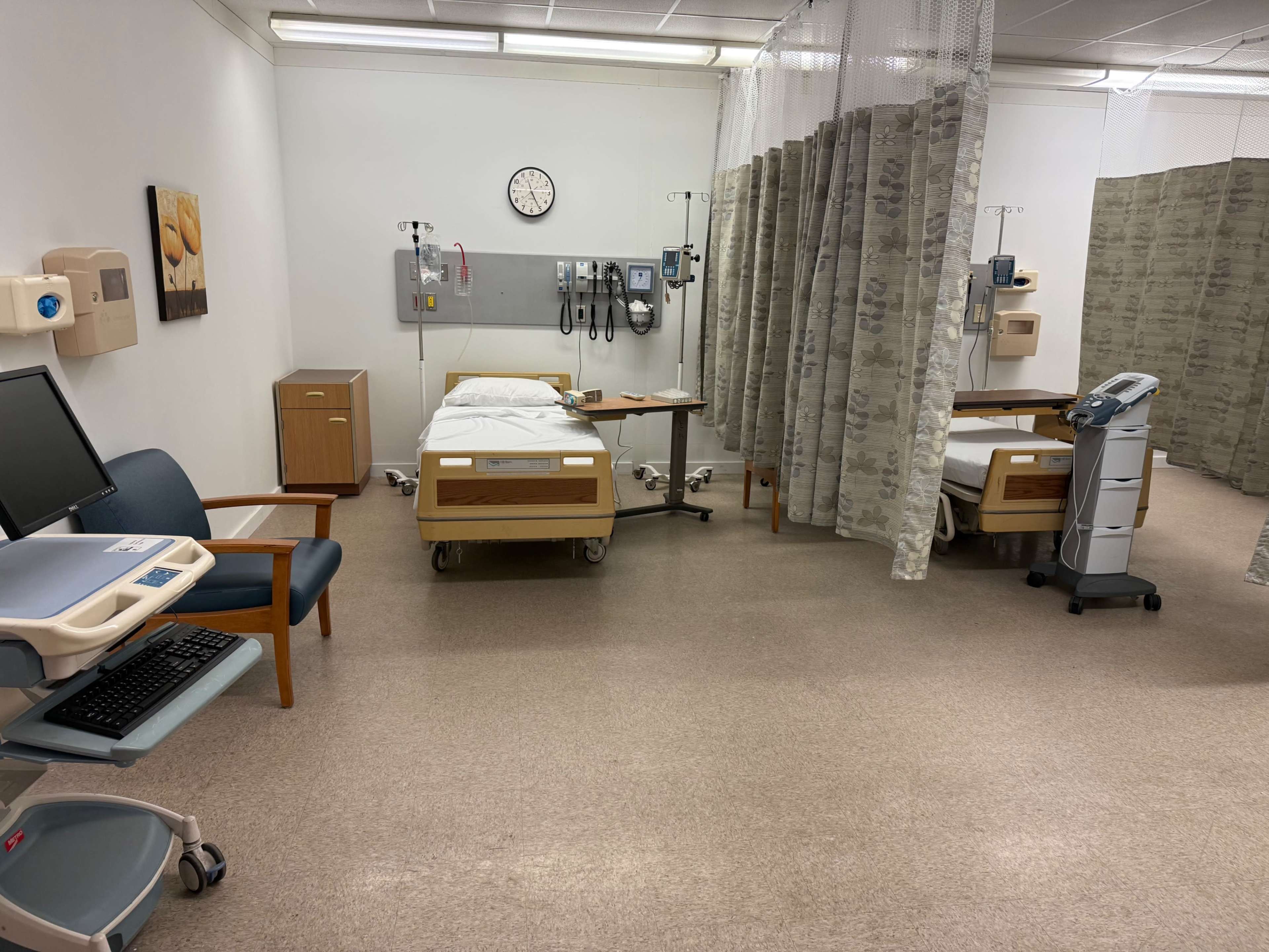 The image shows a hospital room with two patient beds, medical equipment, a computer station, and privacy curtains separating the beds.
