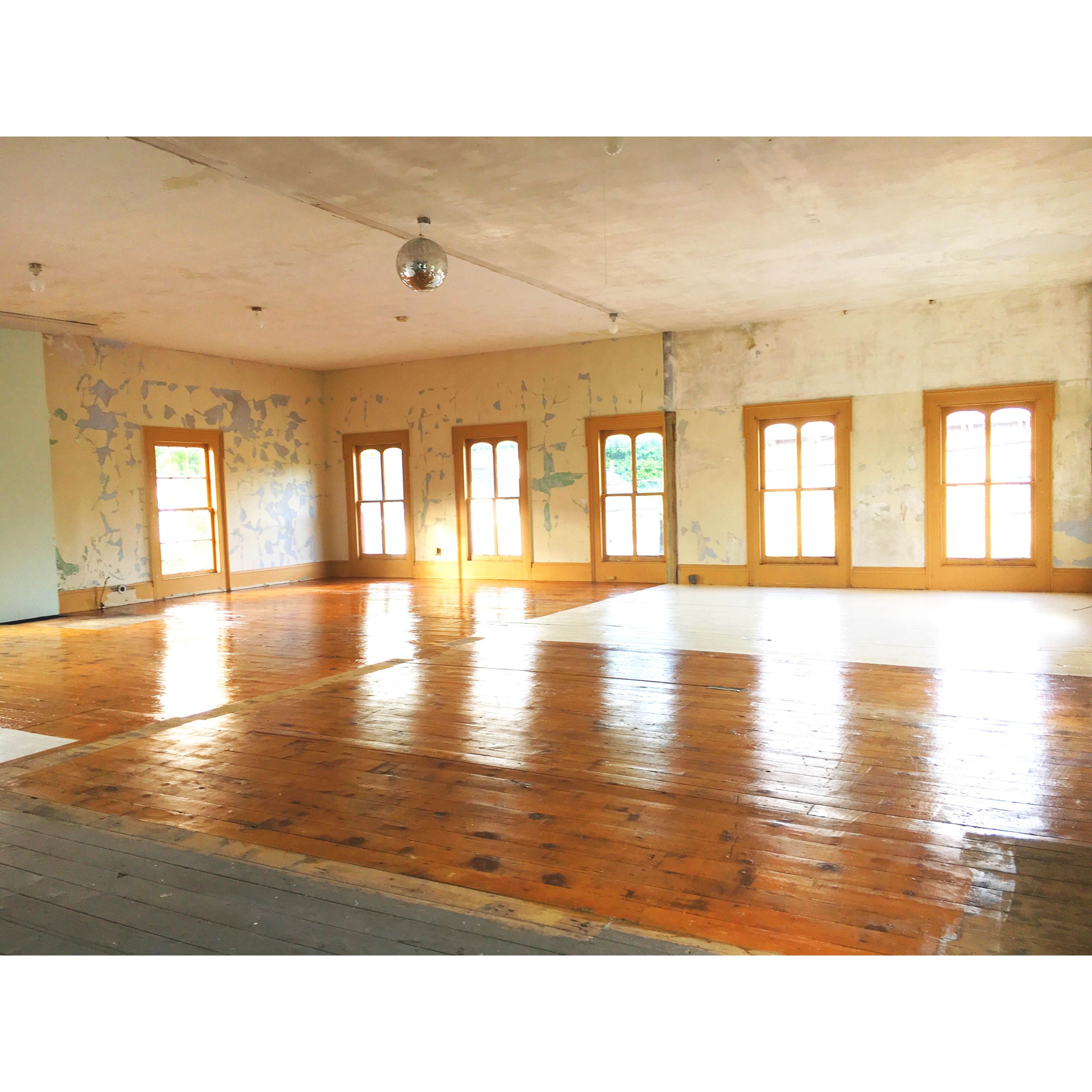 A spacious room with wooden floors, several windows, and peeling paint on the walls.