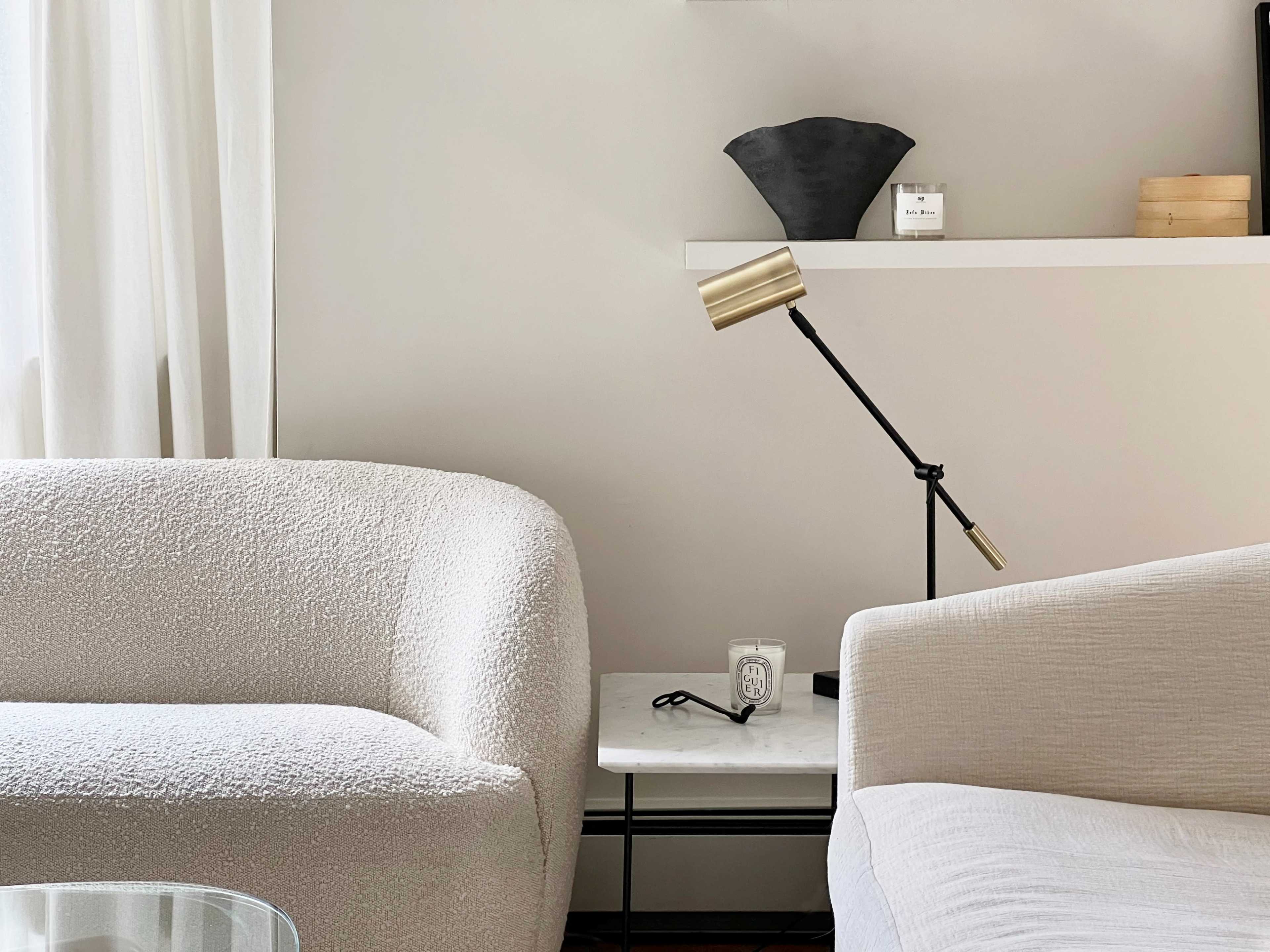 A modern living room features two textured sofas, a black lamp on a marble side table, and decorative objects on a shelf.