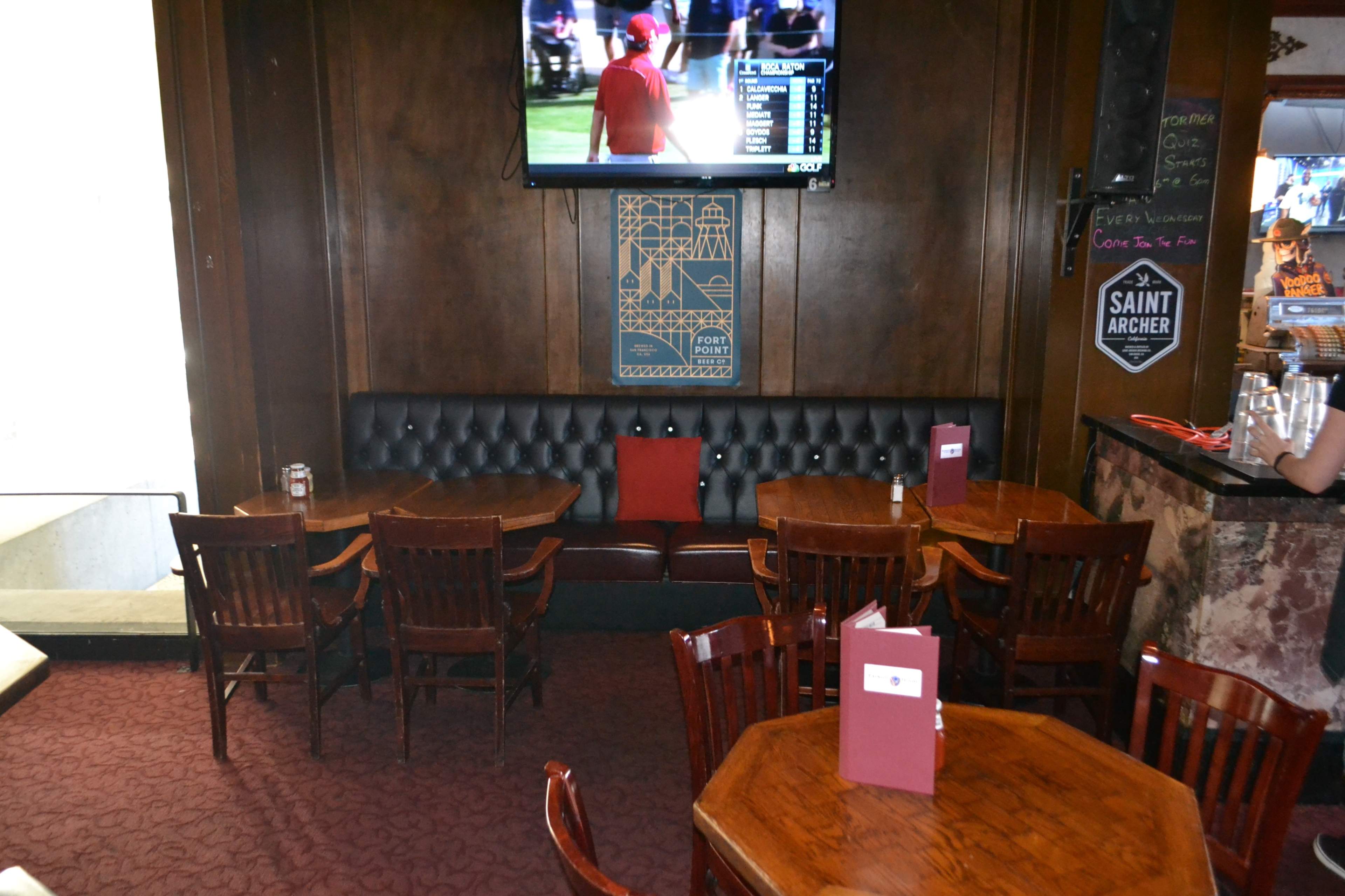 A dimly lit pub with wooden tables, a booth seating area, and a large television displaying a sports game on the wall.
