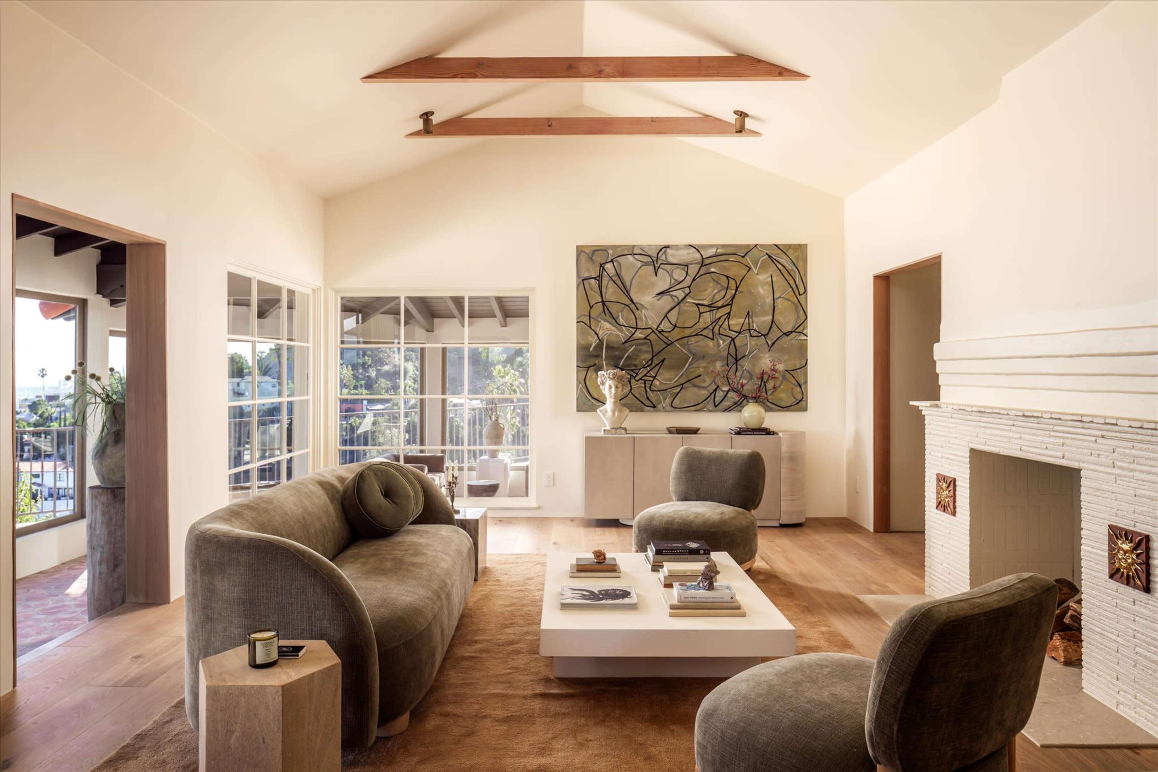 The image shows a modern living room with a high ceiling, featuring a large abstract painting, a central coffee table, and comfortable seating arrangements.