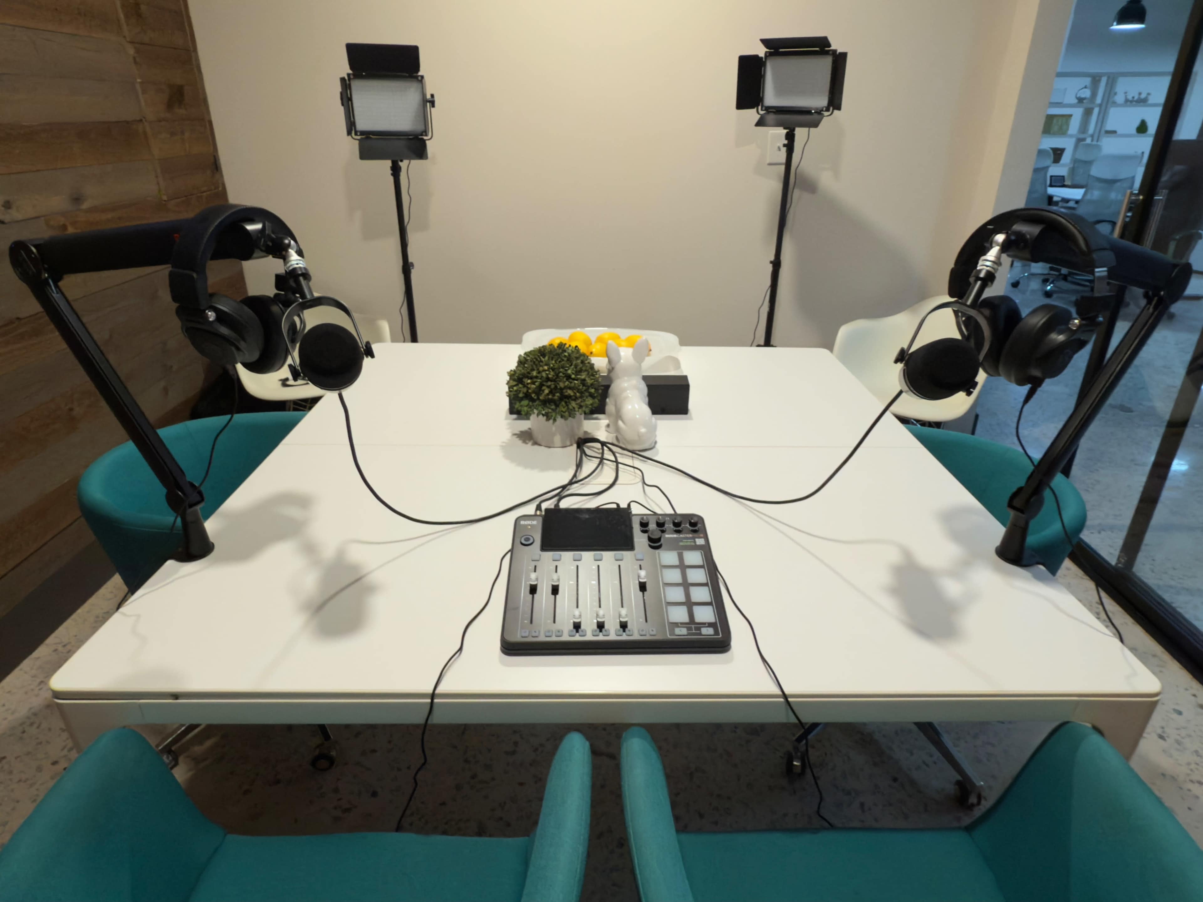 A modern podcast recording setup featuring a table with two microphones and headphones, surrounded by chairs, and equipped with audio mixing equipment.