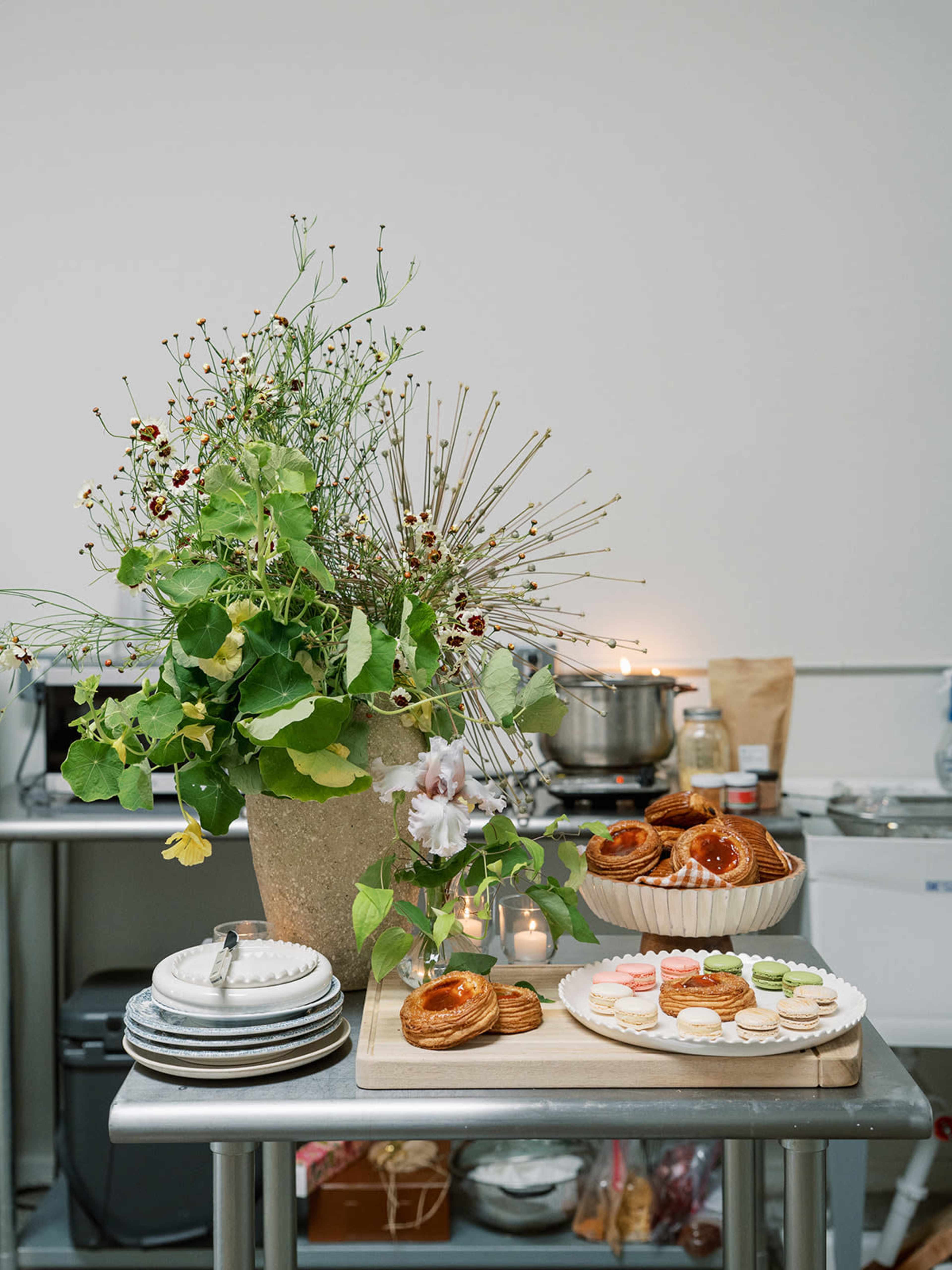 A table is set with an arrangement of pastries, plates, and a large floral centerpiece.