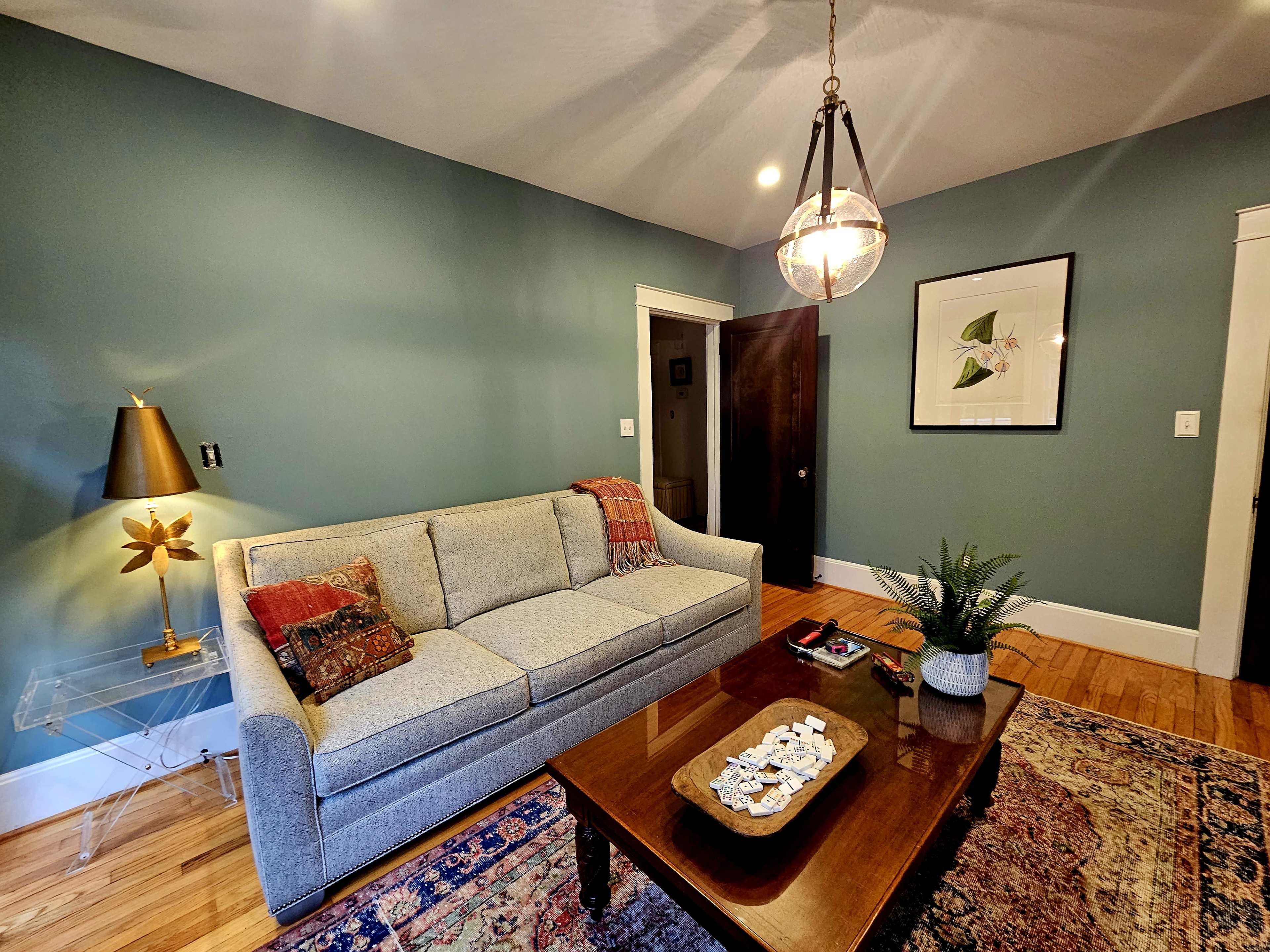 The living room features a gray sofa, a wooden coffee table, and a decorative rug on a hardwood floor, with walls painted in a muted blue color.