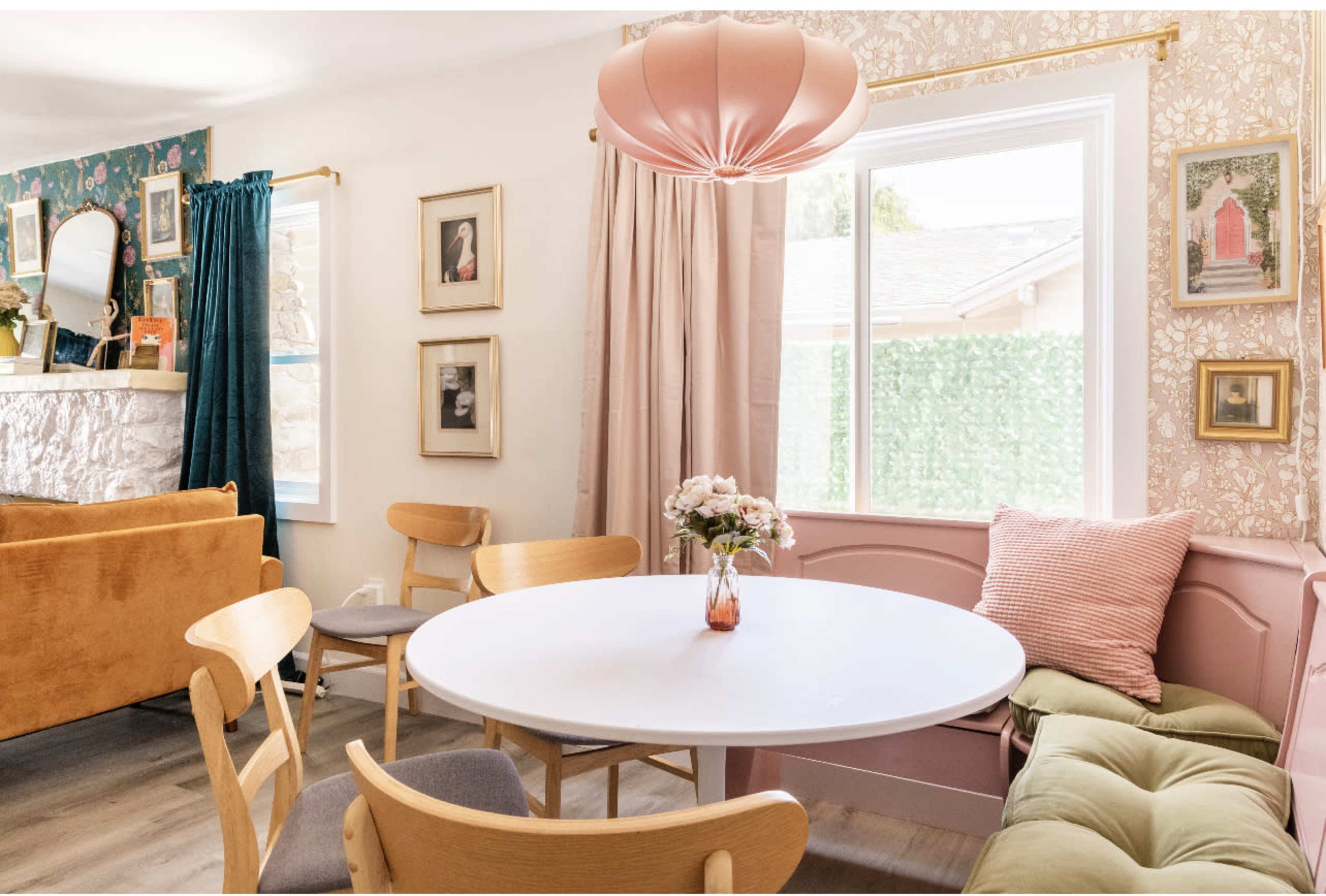A cozy dining area with a round white table surrounded by wooden chairs, a pastel-colored couch, and decorative wall art.