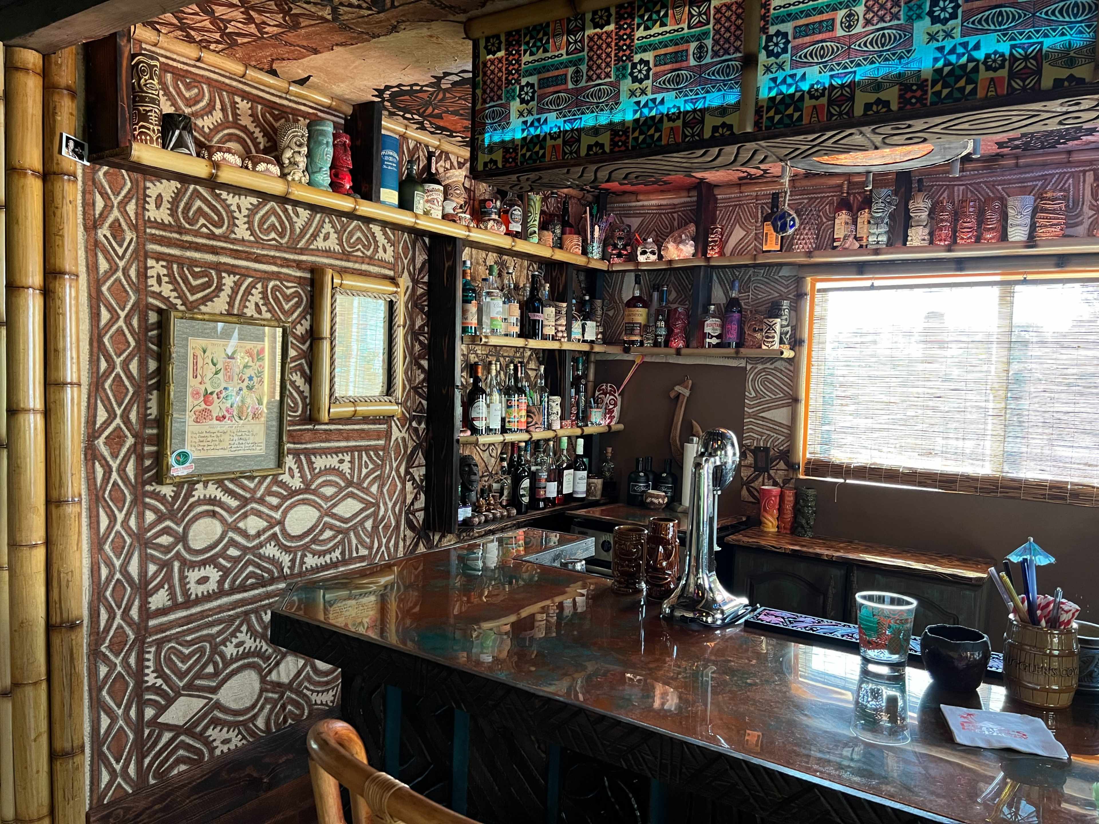 A bar area with decorative walls, shelves filled with various liquor bottles, and a wooden countertop.