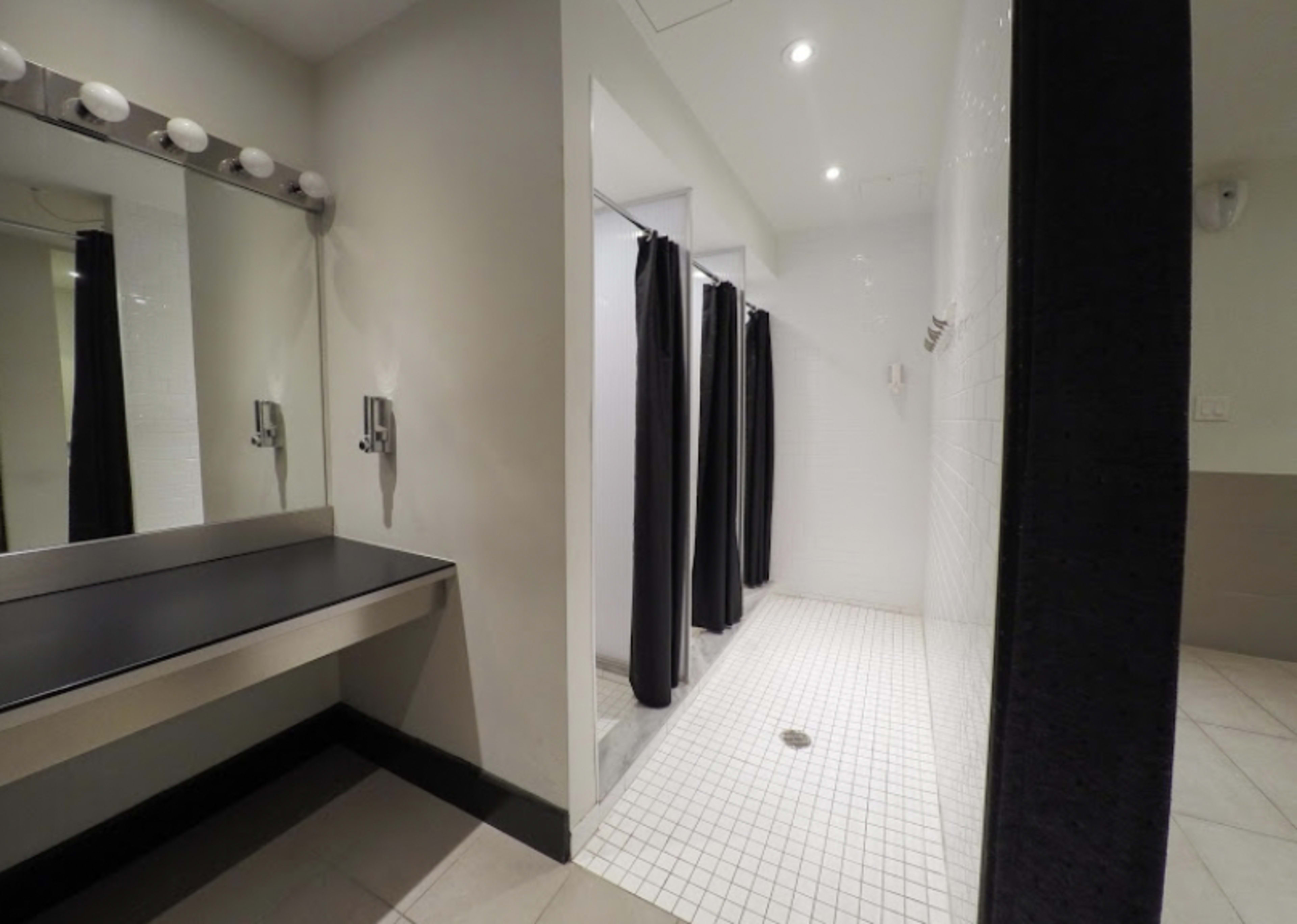 The image shows a bathroom with a changing area that includes a counter with lights and two separate shower stalls with dark curtains.