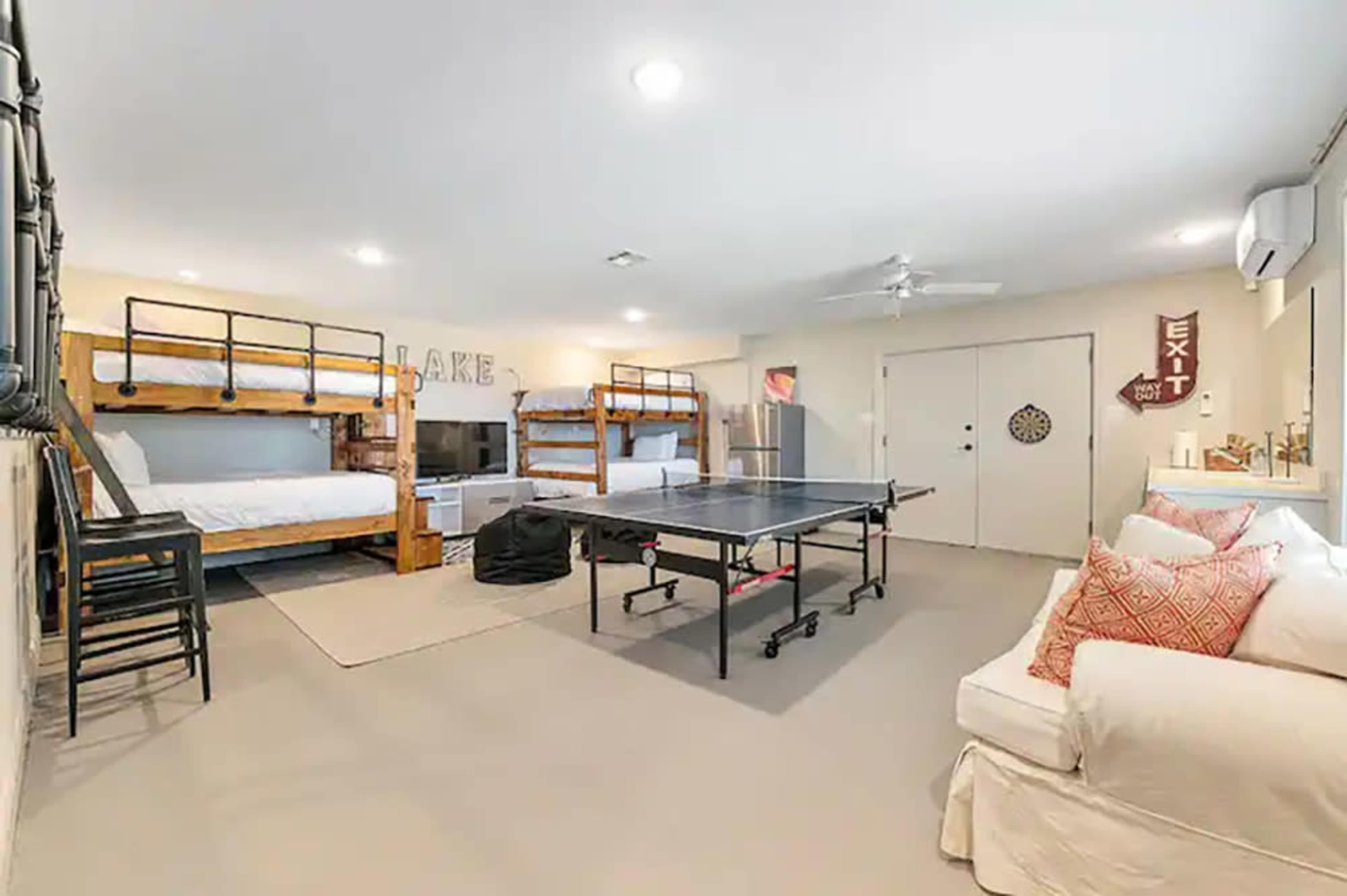 A spacious room with bunk beds on one side, a ping-pong table in the center, and a sofa with decorative pillows on the opposite side.