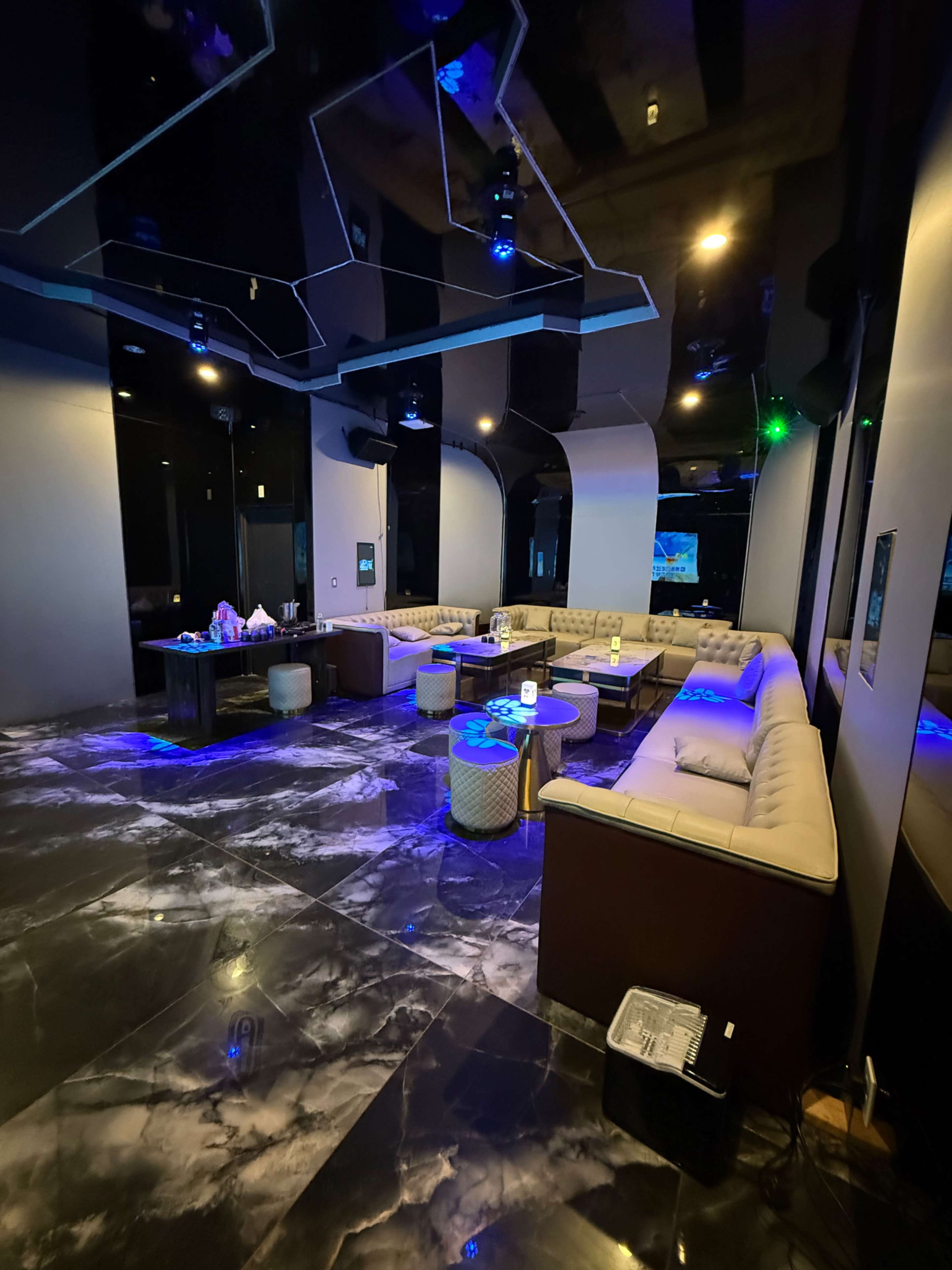 The image shows a modern lounge area with plush seating, a dark marble floor, and ambient lighting designed for social gatherings.