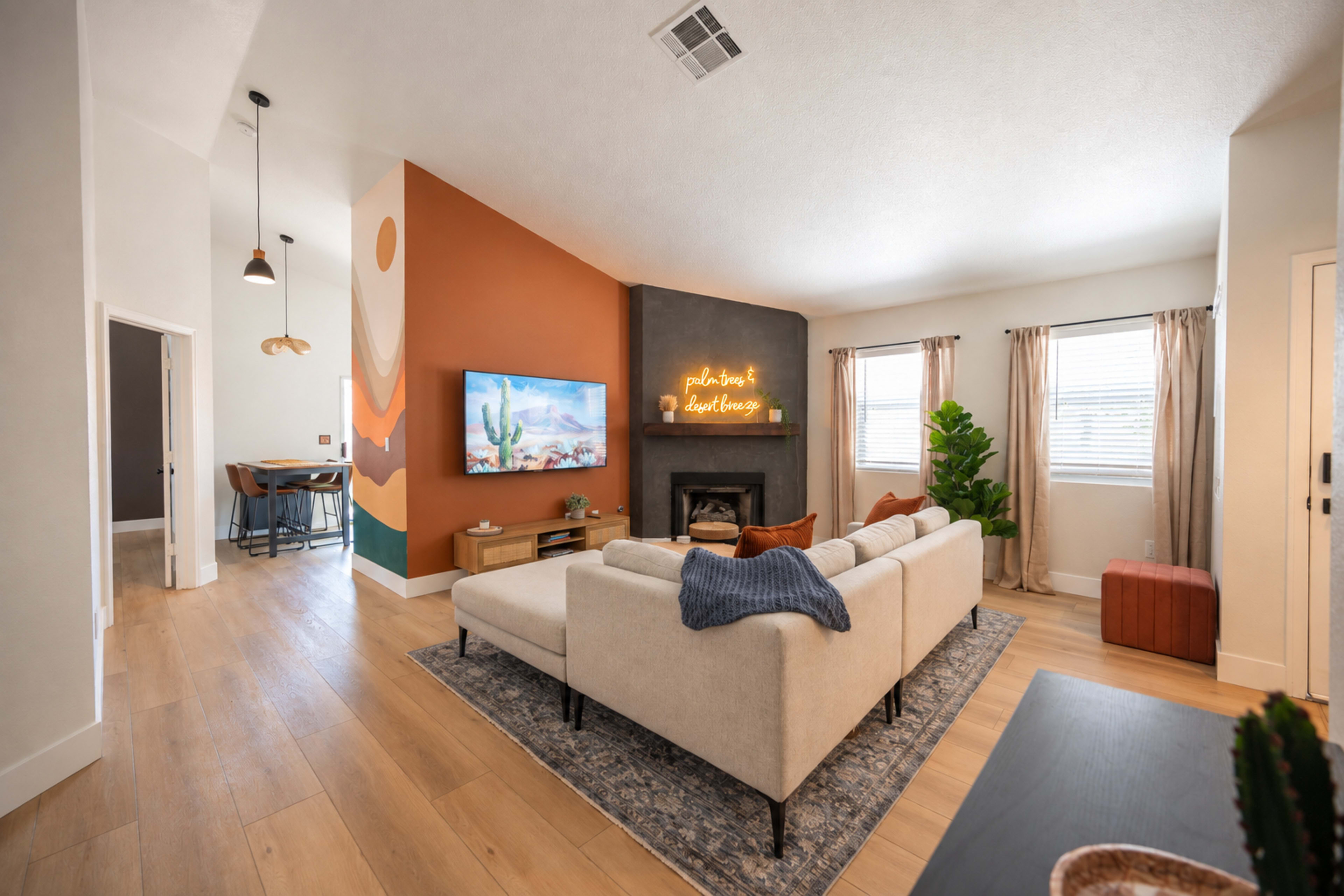 The living room features a light-colored sectional sofa facing a mounted television and a fireplace, with an accent wall painted in orange and gray.