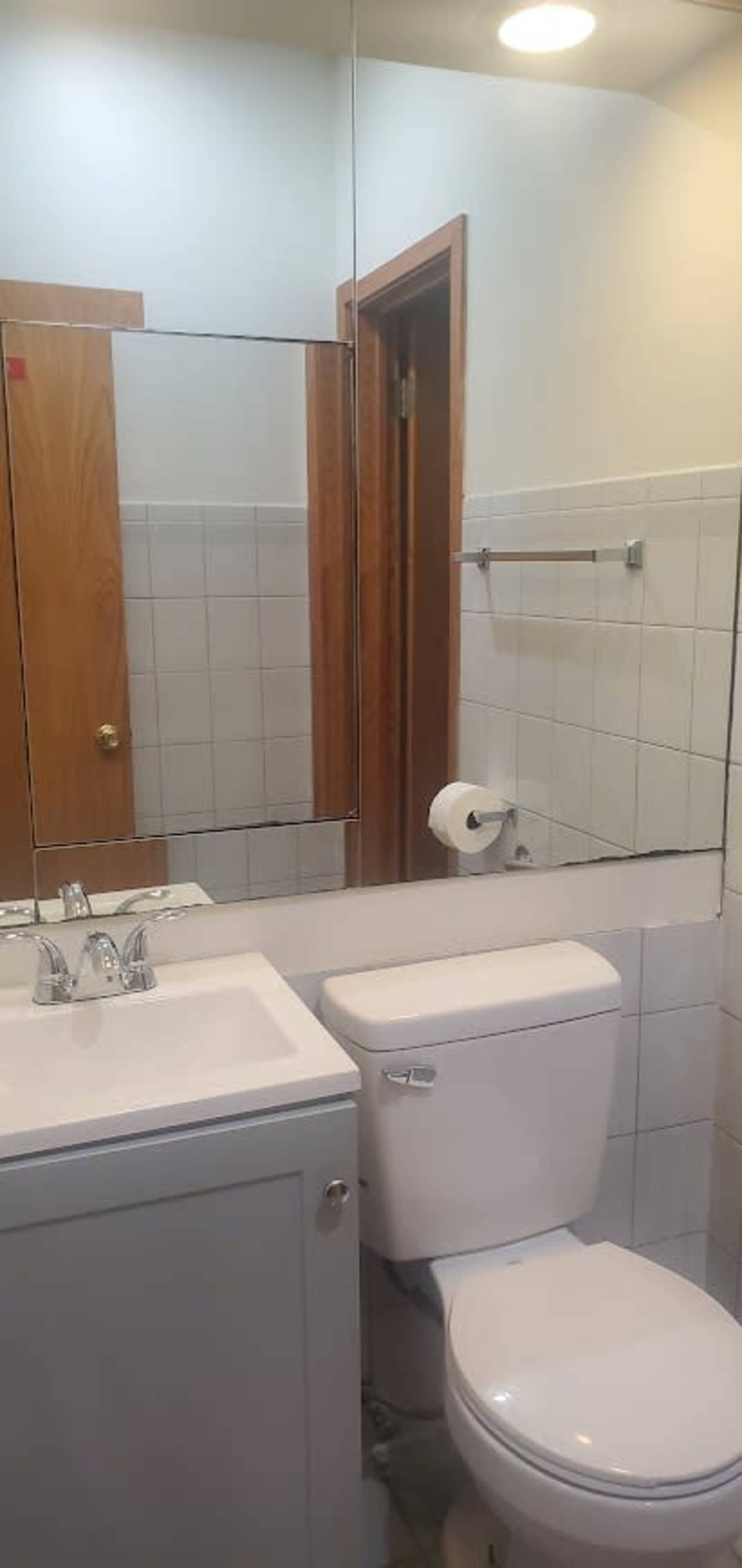 A bathroom with a sink, toilet, and a large mirror above the sink, featuring tiled walls and a wooden door.
