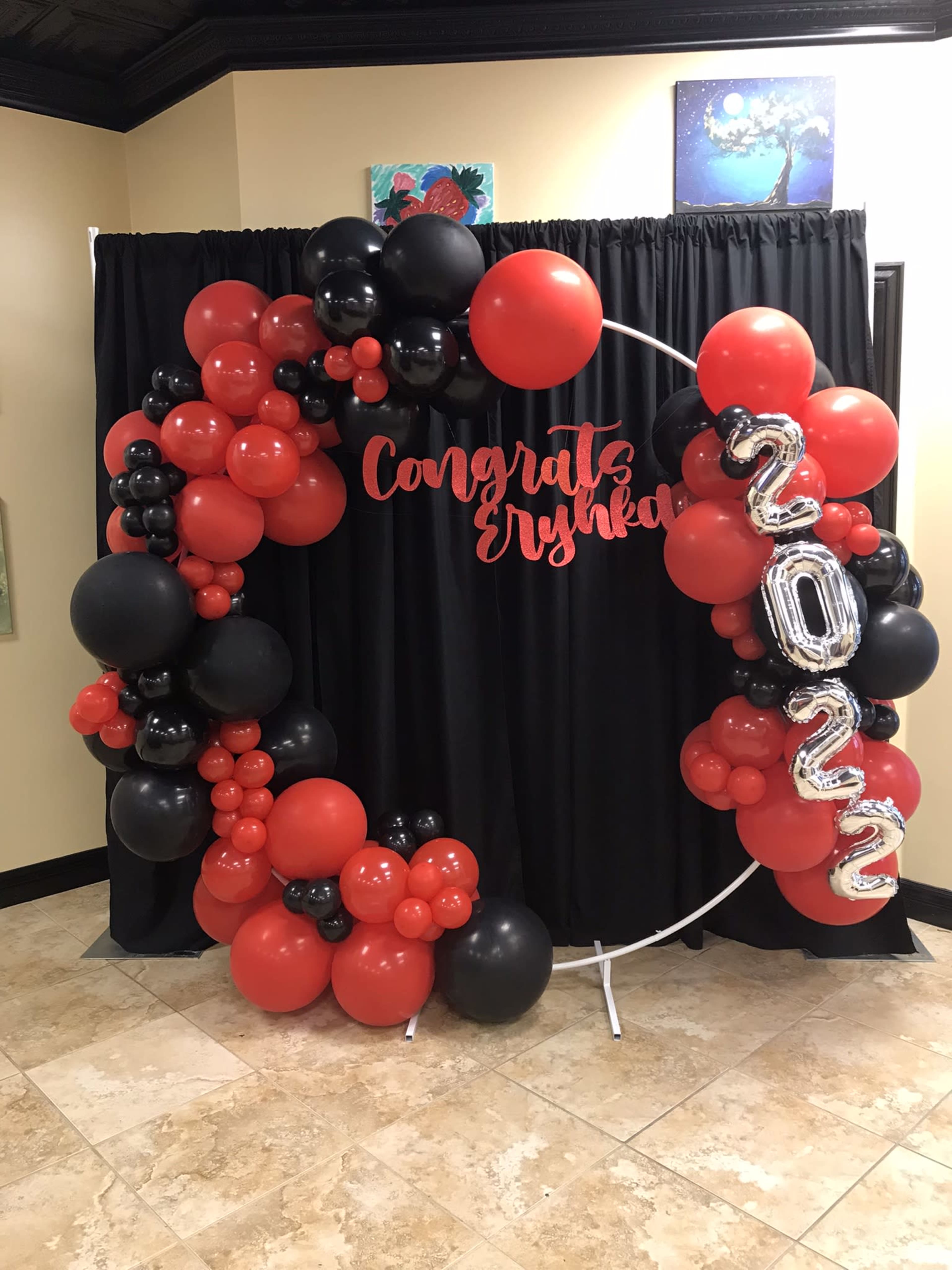 A decorative arch made of red, black, and silver balloons, with a "Congrats Erynka 2022" sign, set against a black backdrop.
